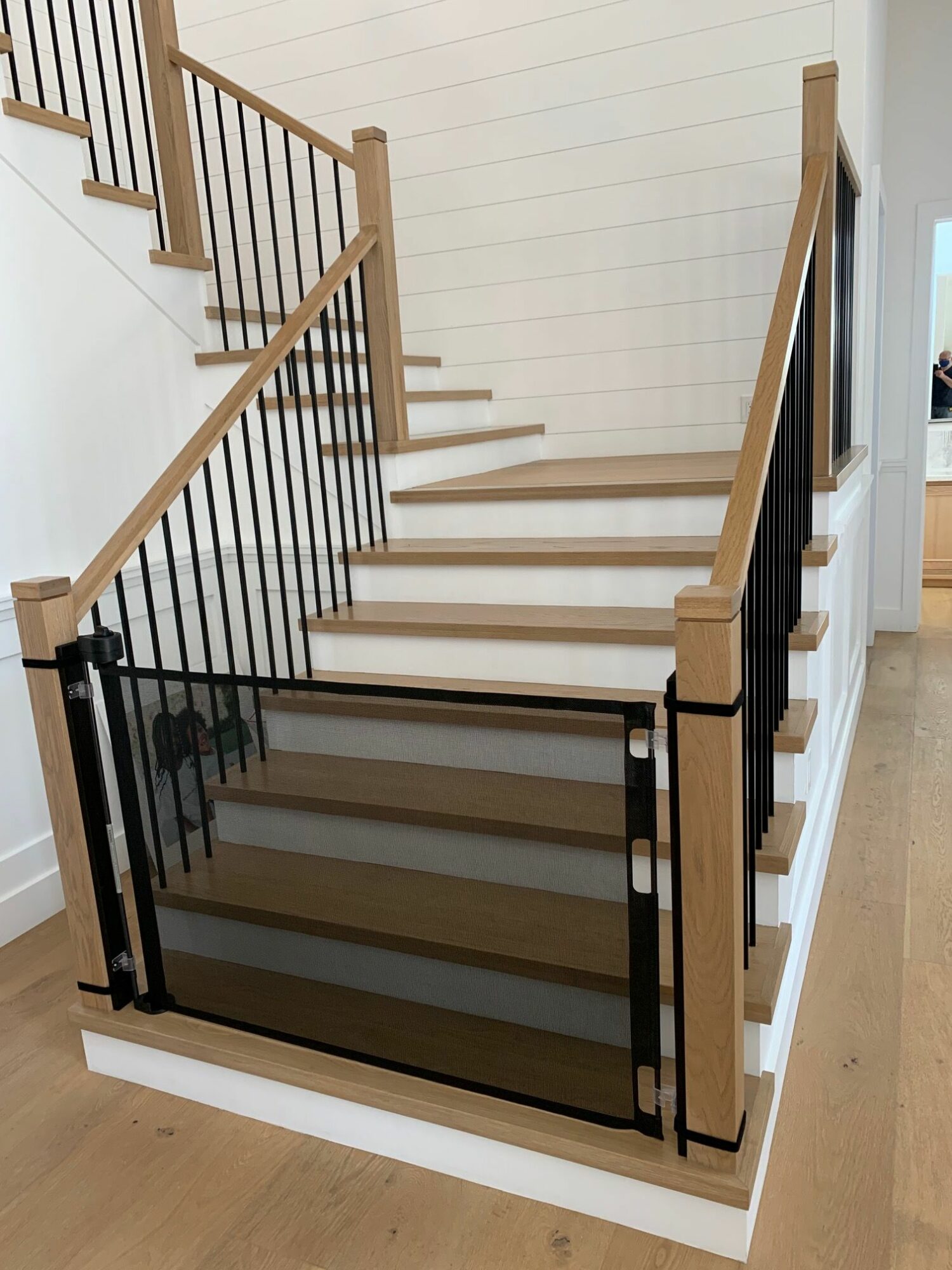 View of a staircase with wooden steps and black metal railings, seen from above, with a glass door at the bottom.