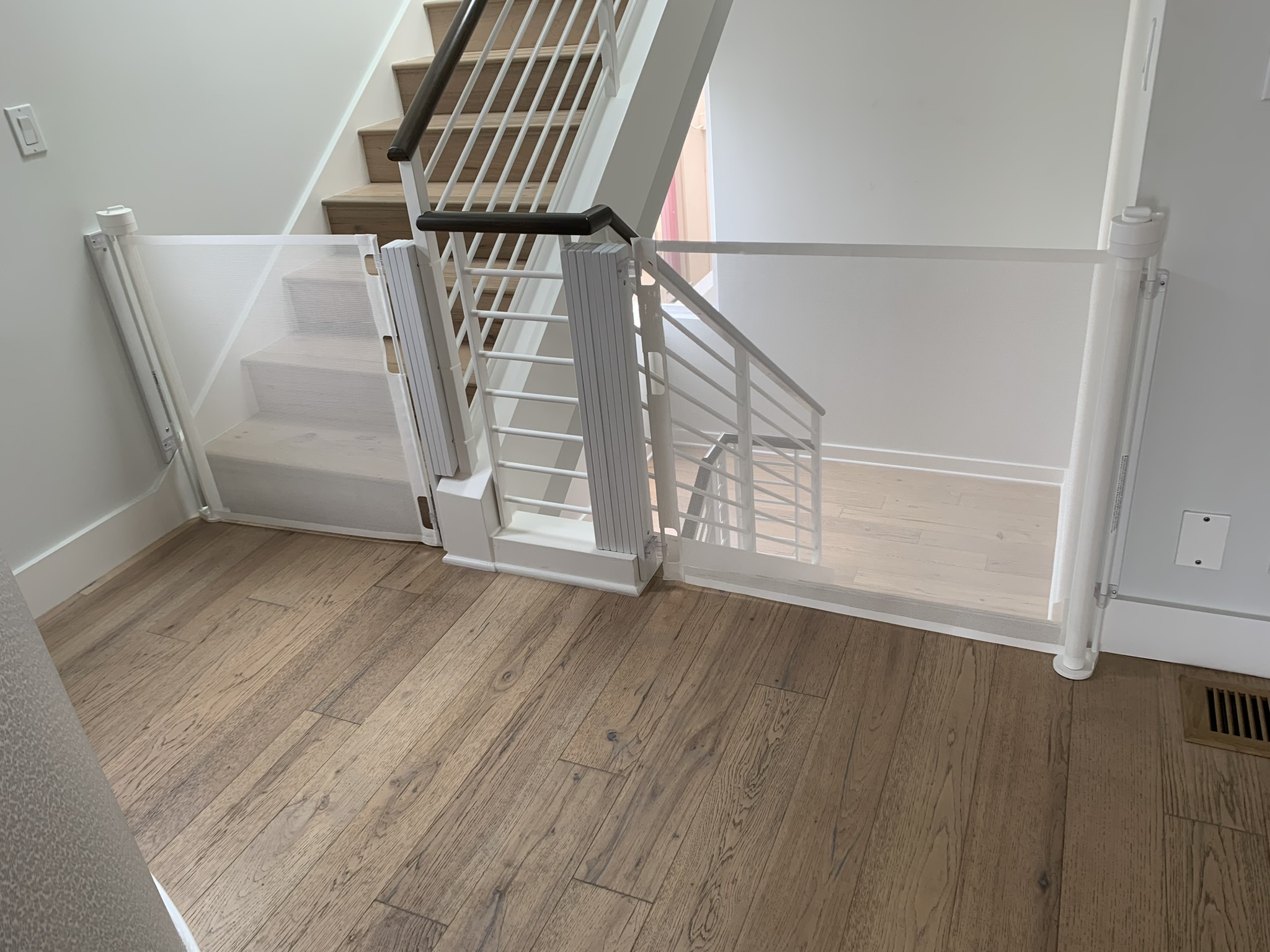 View of staircase with safety gate at top, wooden floor, white walls, and staircase leading down.