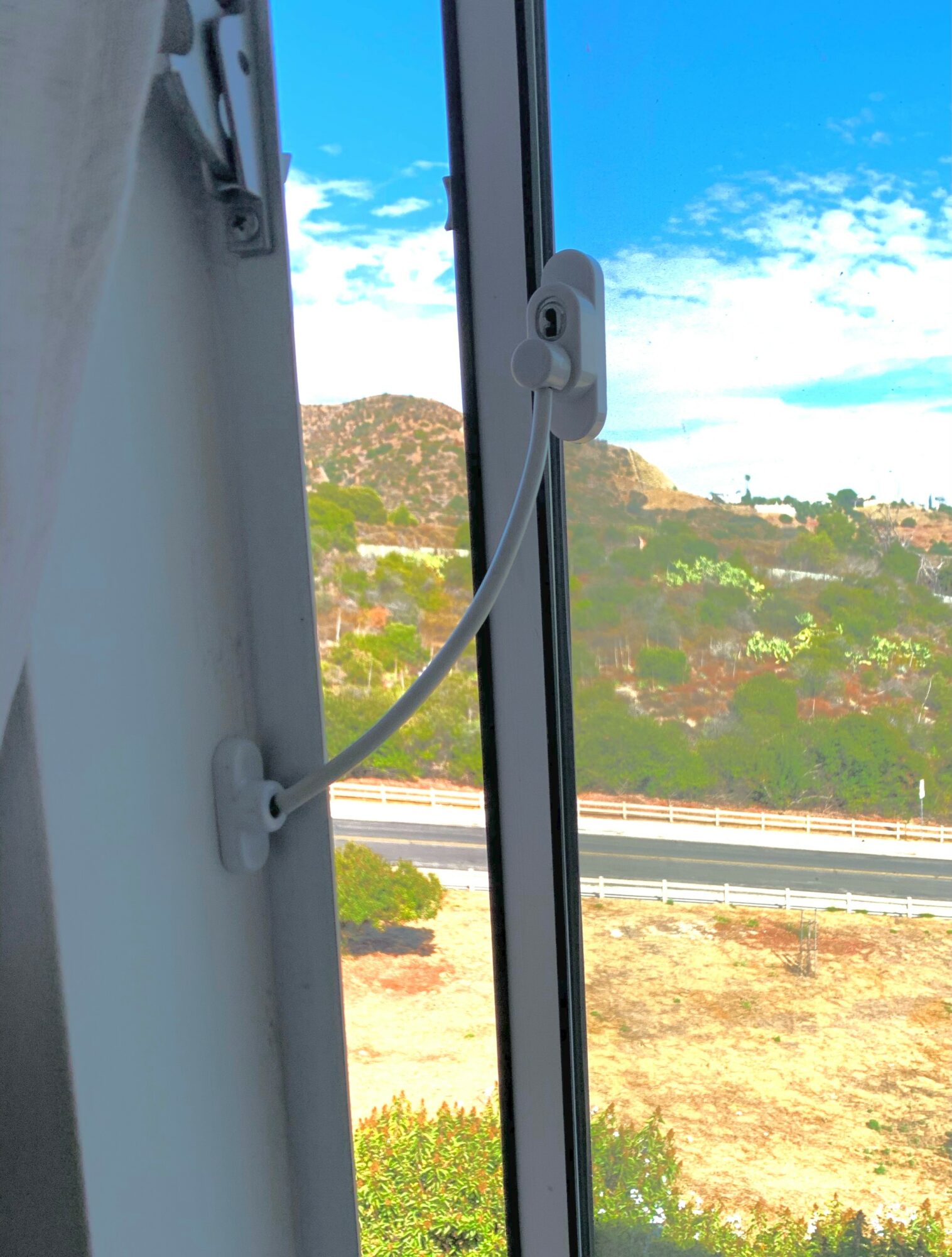 View through a window showing a landscape with hills, a highway, and a partly cloudy sky.
