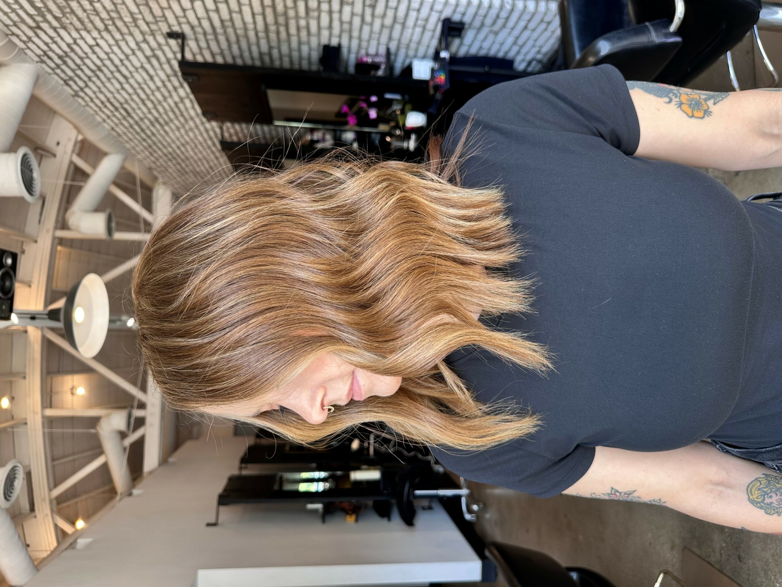 Side view of a woman with wavy, shoulder-length hair, wearing a black shirt, in an indoor setting.