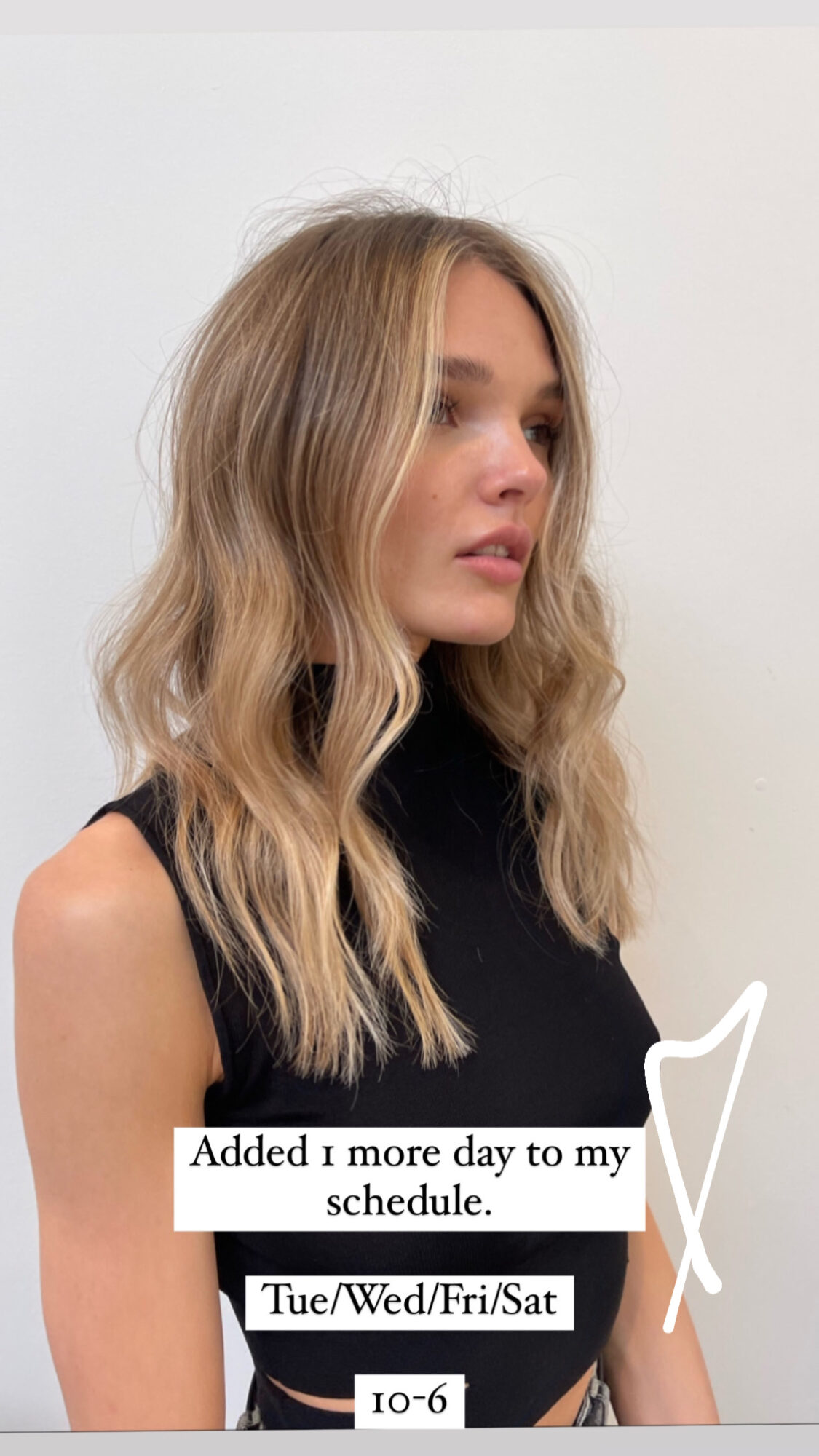Young woman with wavy blonde hair wearing a black sleeveless top, looking to the side, against a plain background.