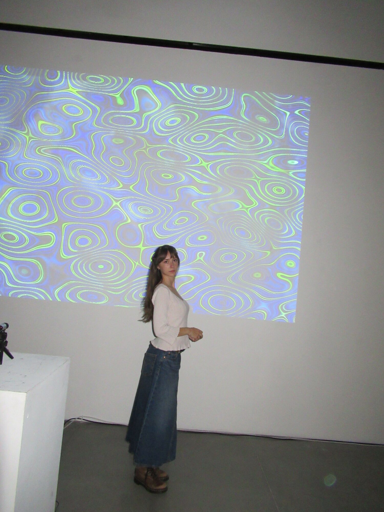 Person standing in front of a wall with colorful, abstract patterns projected on it.