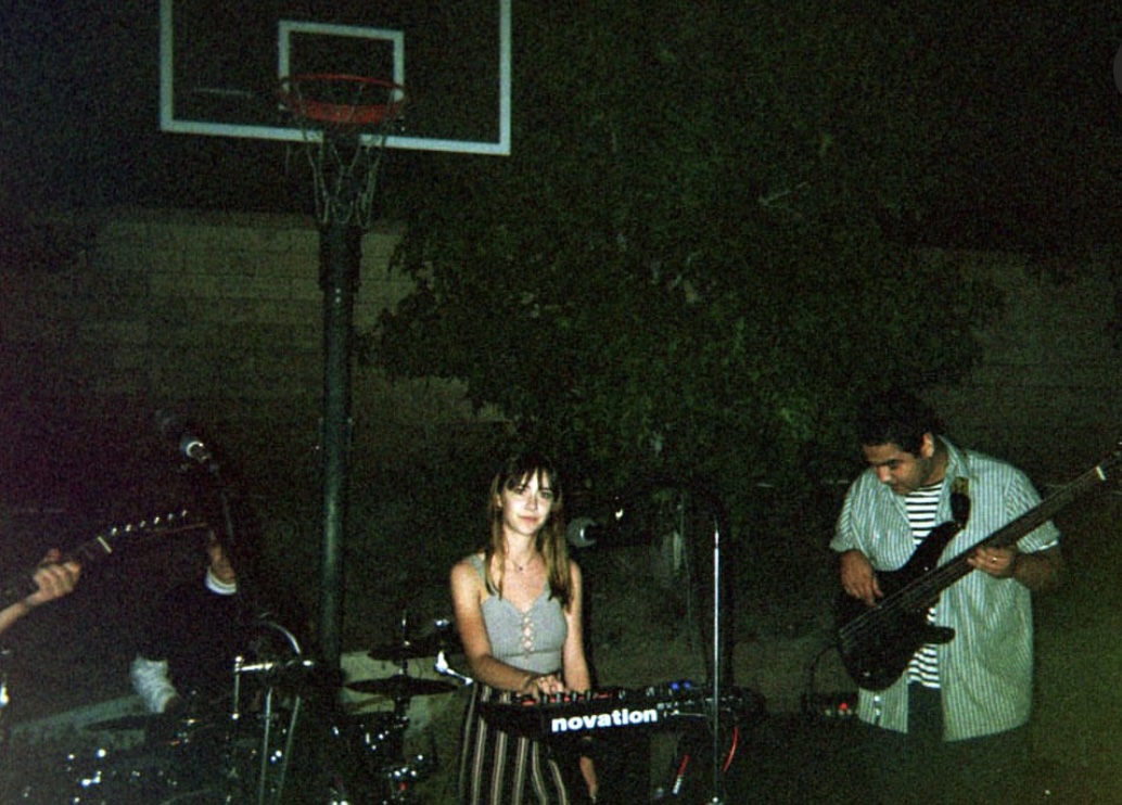 Three people playing musical instruments outdoors at night, with a basketball hoop in the background.