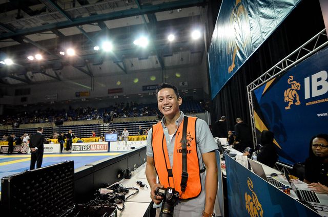 Person wearing an orange vest smiling at a sports event, with a camera hanging around their neck, in an indoor arena.