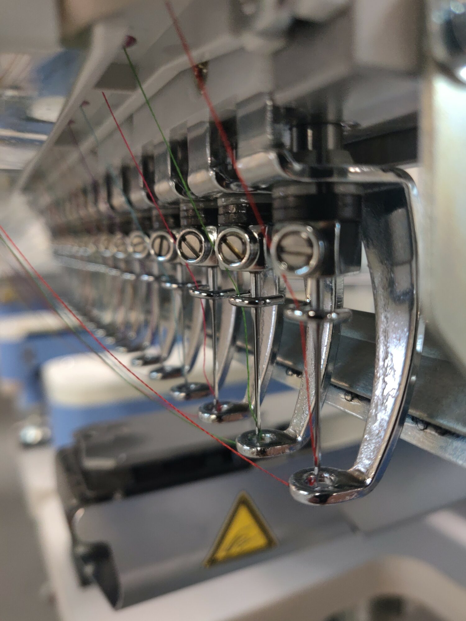 Close-up of industrial sewing machine with metal components and red thread, viewed from the side.