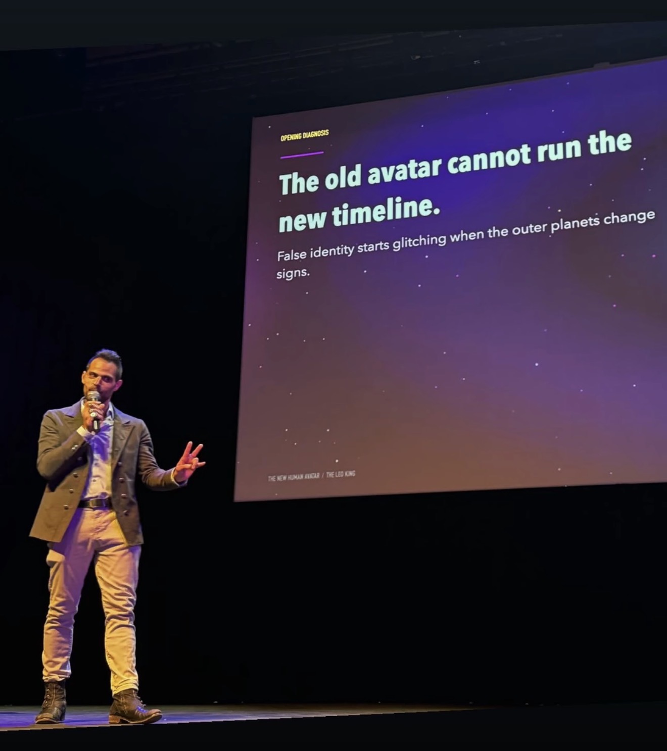 Person in a suit speaking on stage with a presentation slide behind them, displaying text about avatars and timelines.