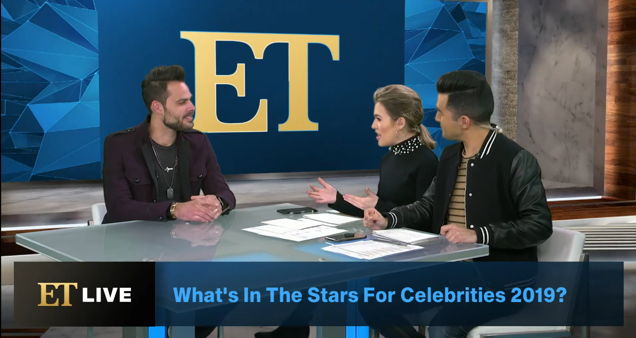 Three people sit at a news desk with an ET logo behind them, discussing celebrities in 2019.