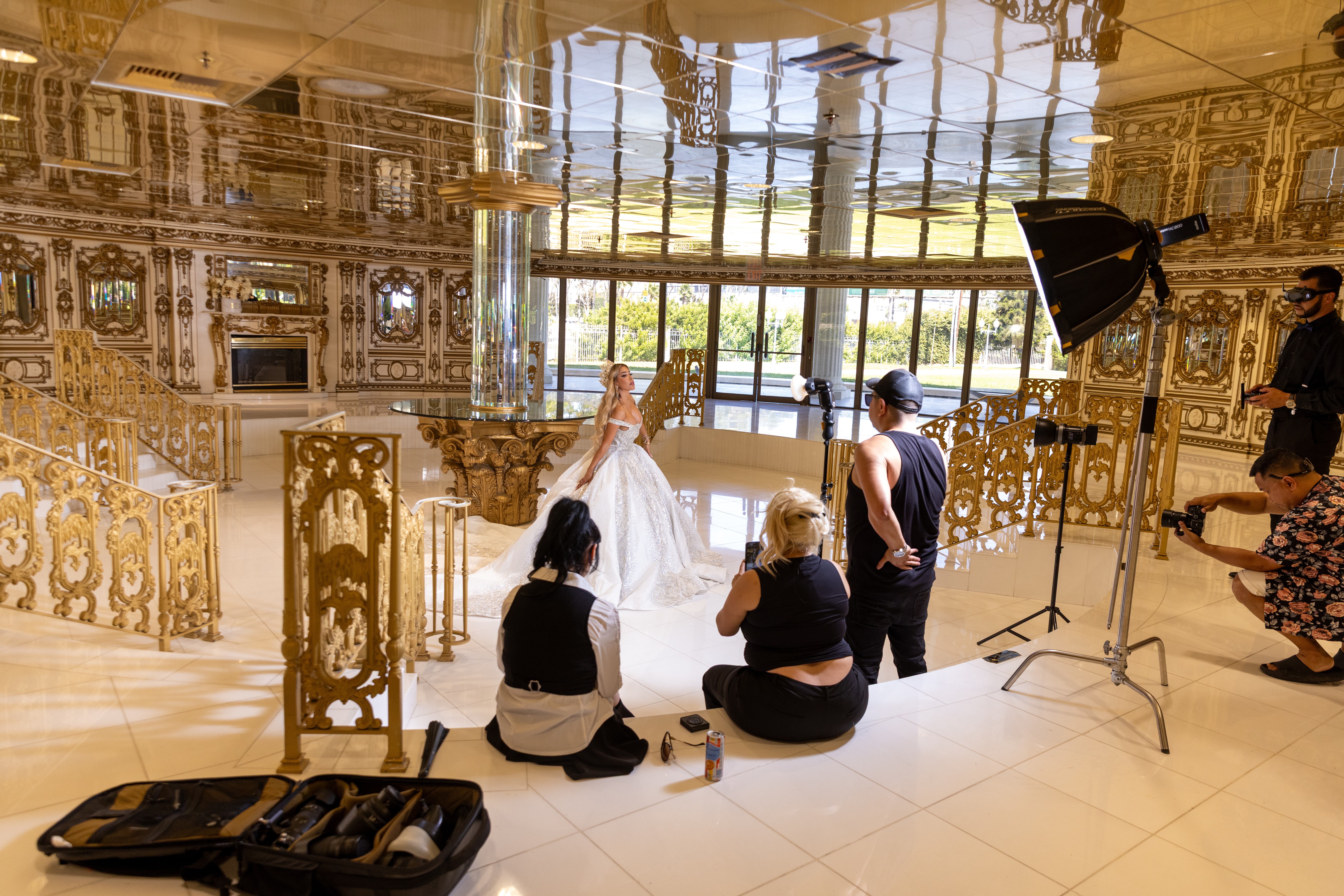People in a luxurious, ornate room with gold accents and large windows, some sitting and others standing, with a photographer and lighting equipment present.