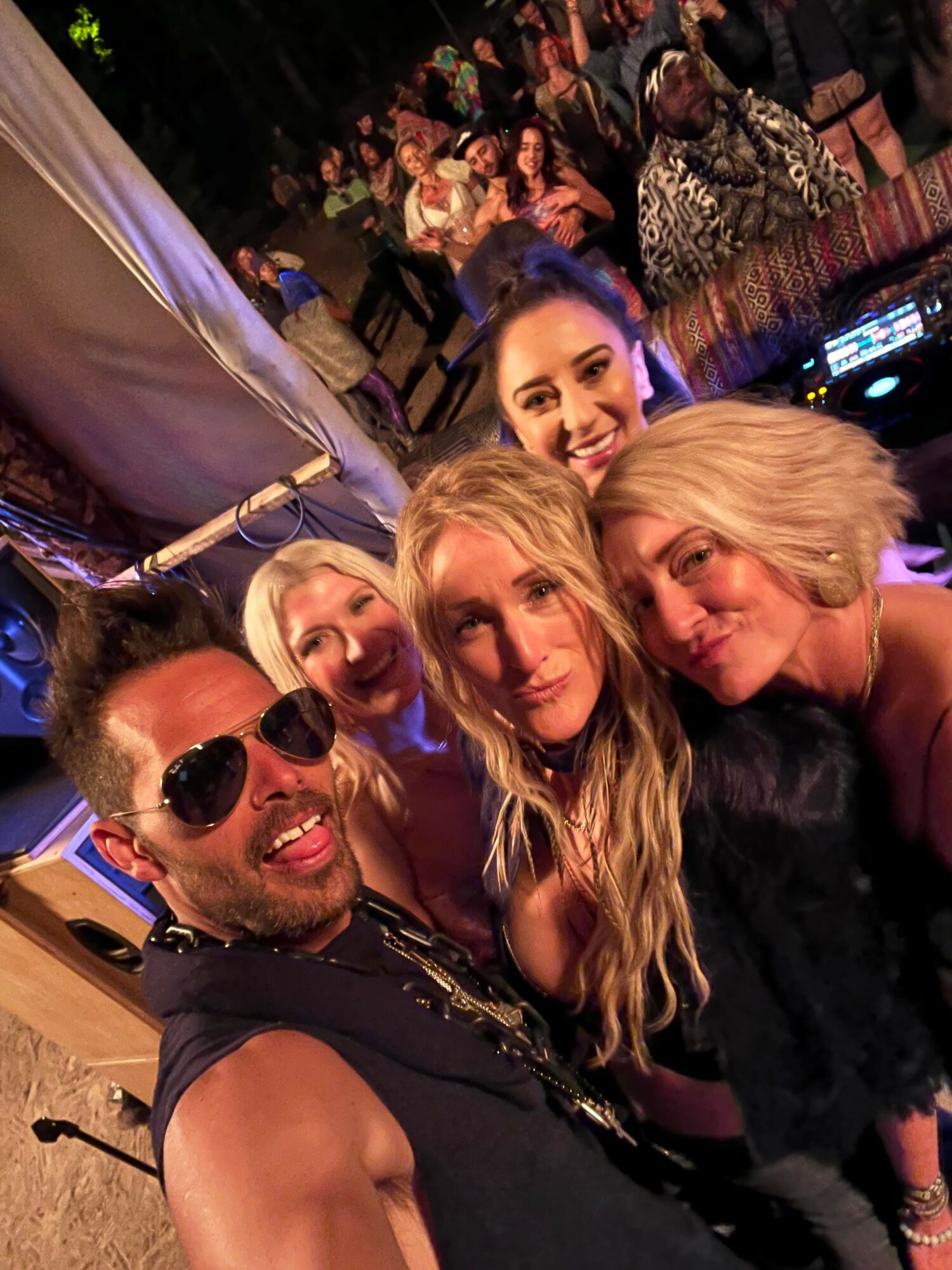 Four people smiling and posing for a photo at a social event, with a lively background and colorful lighting.