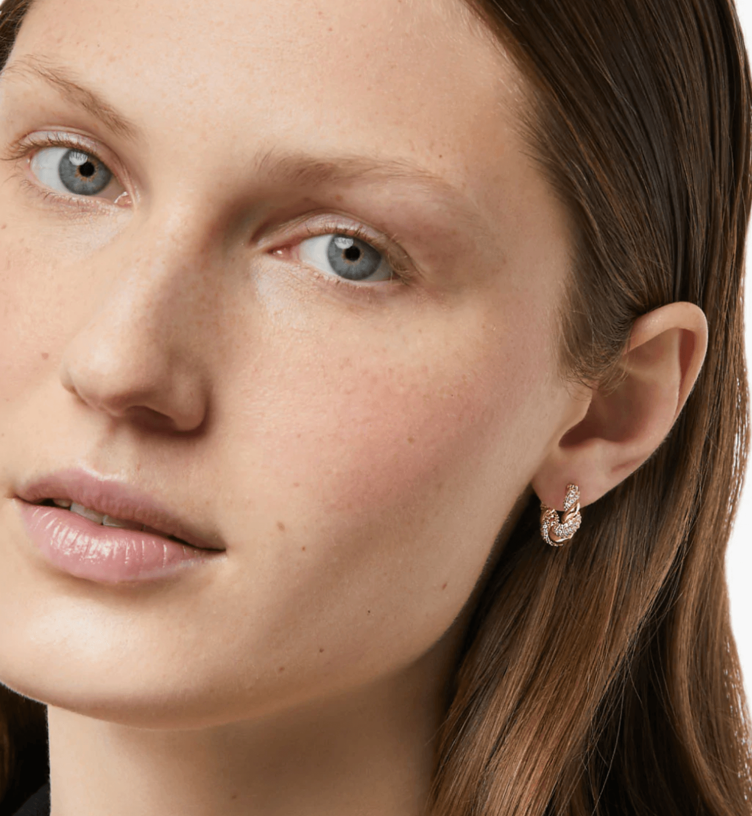 Close-up of a woman with blue eyes, fair skin, and brown hair wearing a small hoop earring, looking slightly to the side.