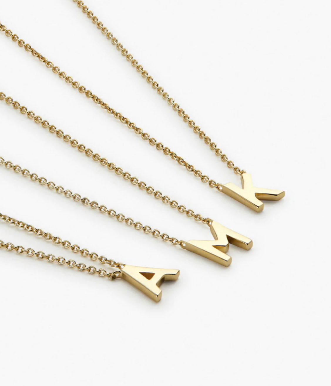 Four gold necklaces with letter pendants spelling A, V, L, and L, arranged diagonally on a white background.