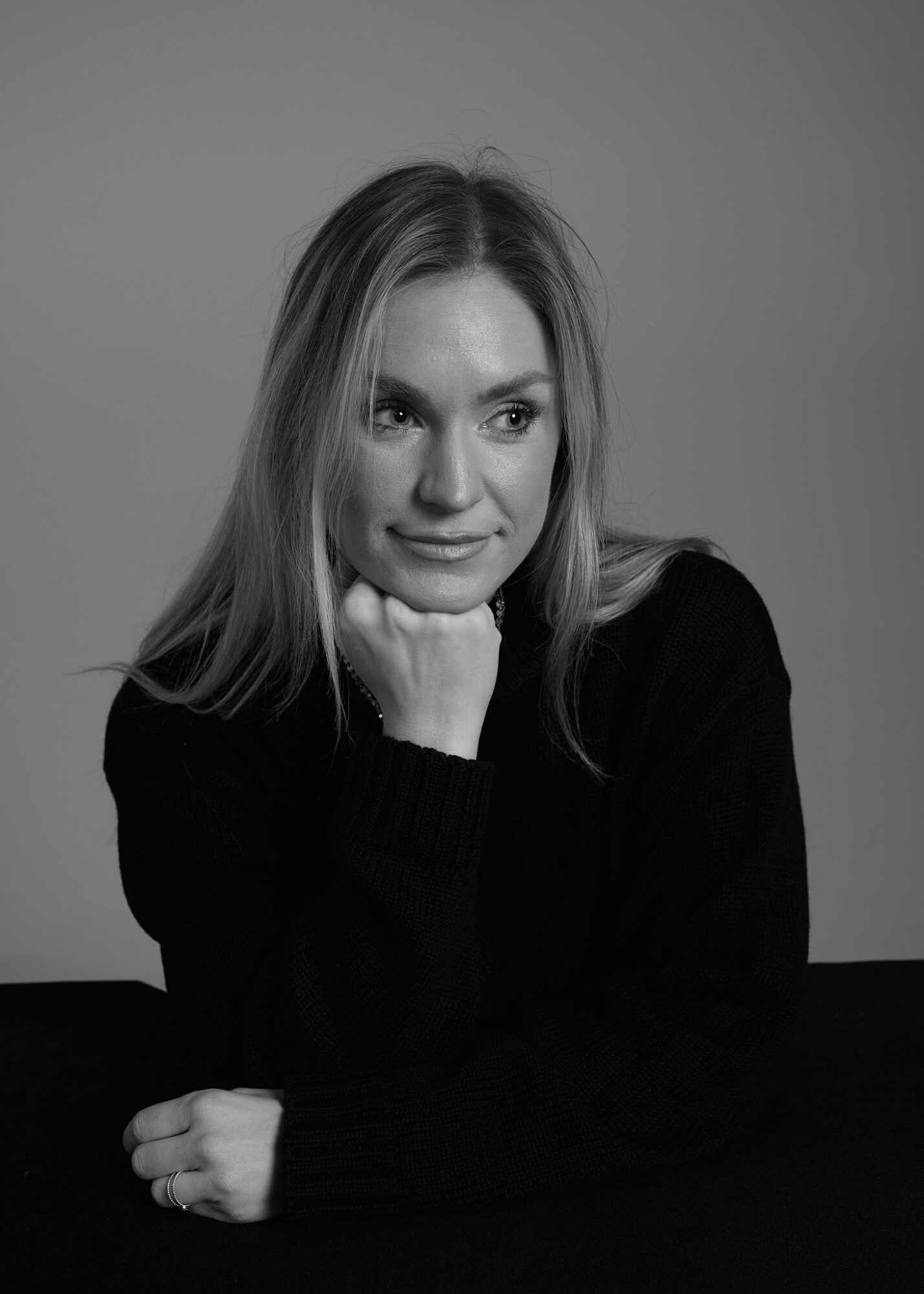 Young woman with long hair resting her chin on her hand, looking to the side, in black and white.
