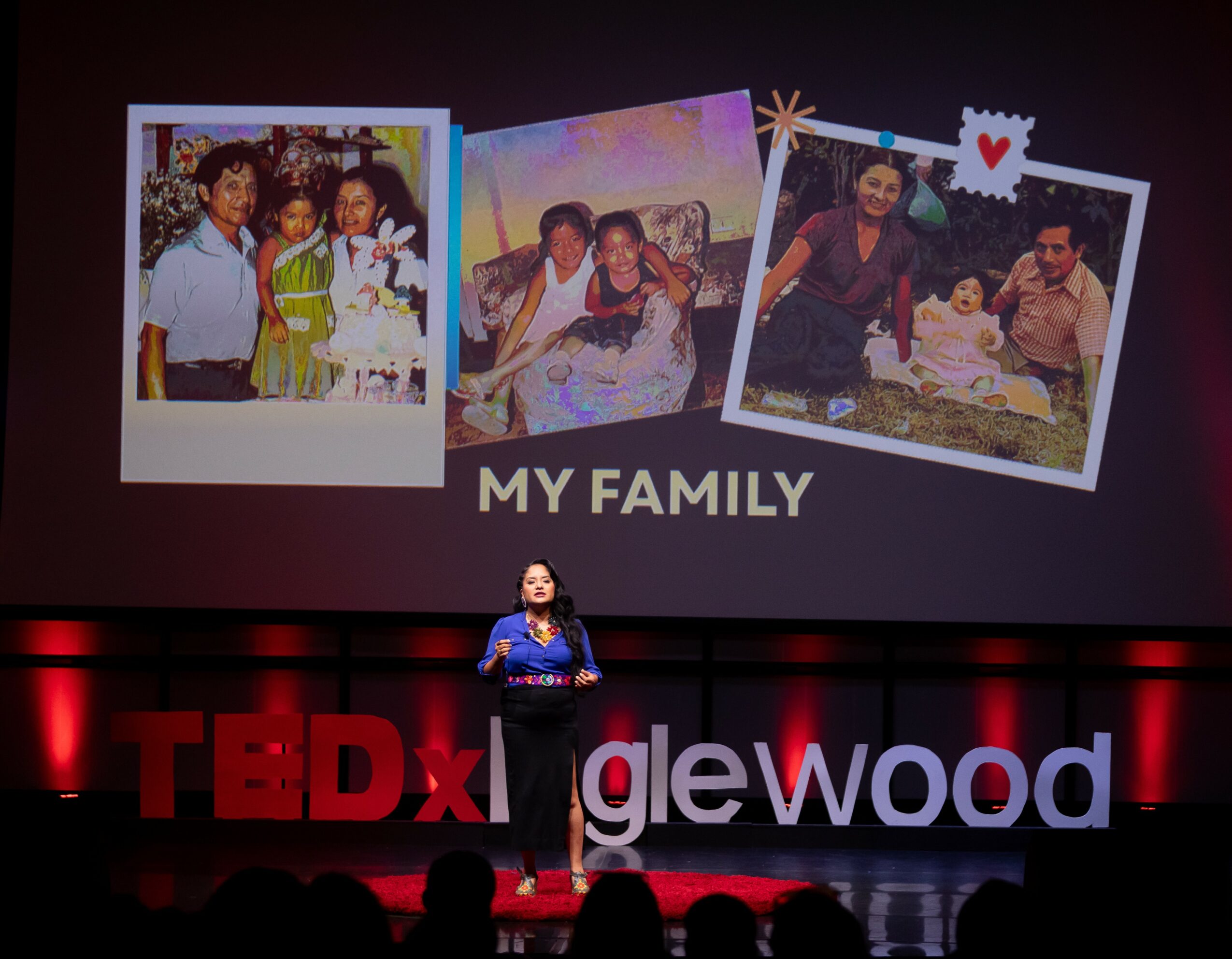 Woman standing on stage with a large screen displaying three family photos and the text 'MY FAMILY'.