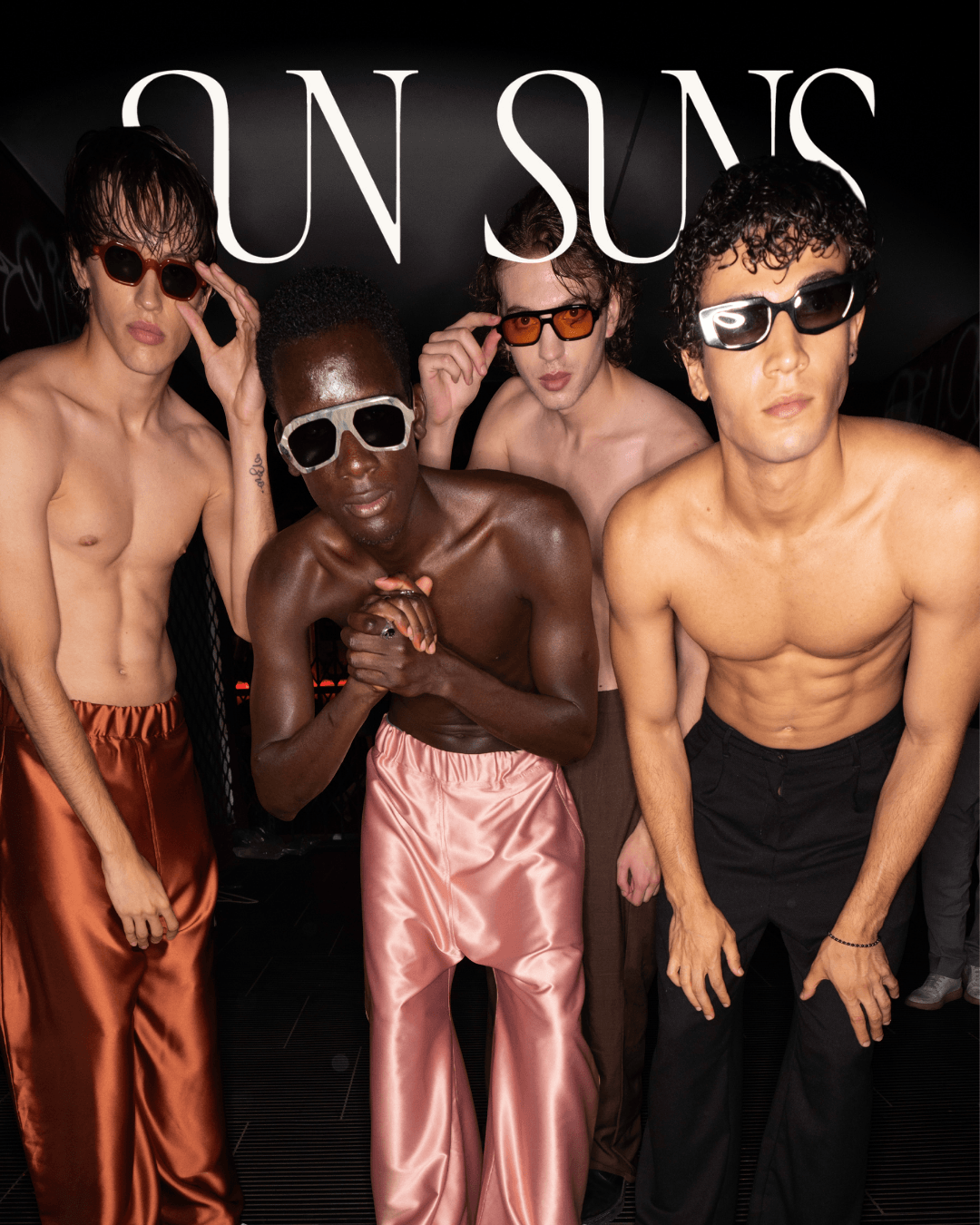 Four shirtless young men wearing sunglasses, standing close together against a dark background.