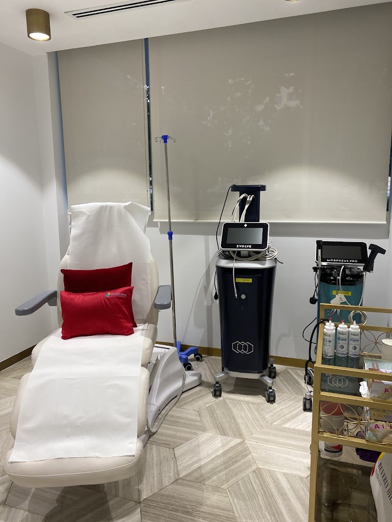 Medical examination room with chair, medical equipment, and supplies, window with closed blinds, and a white wall.