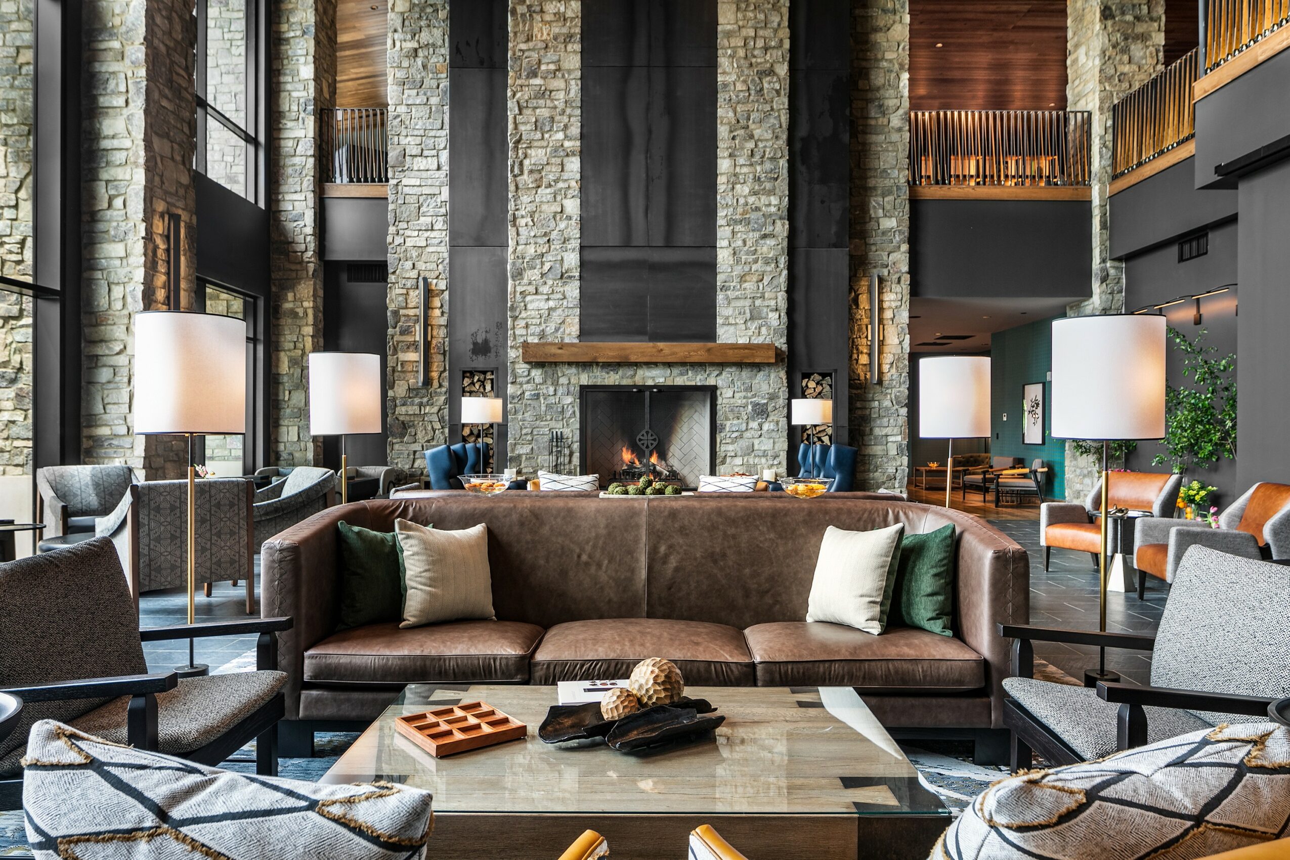Modern hotel lobby with a large sofa, marble coffee table, and tall stone pillars, illuminated by lamps and natural light.