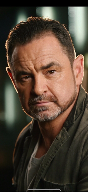 Close-up of a middle-aged man with short dark hair, beard, and serious expression, wearing a dark jacket.