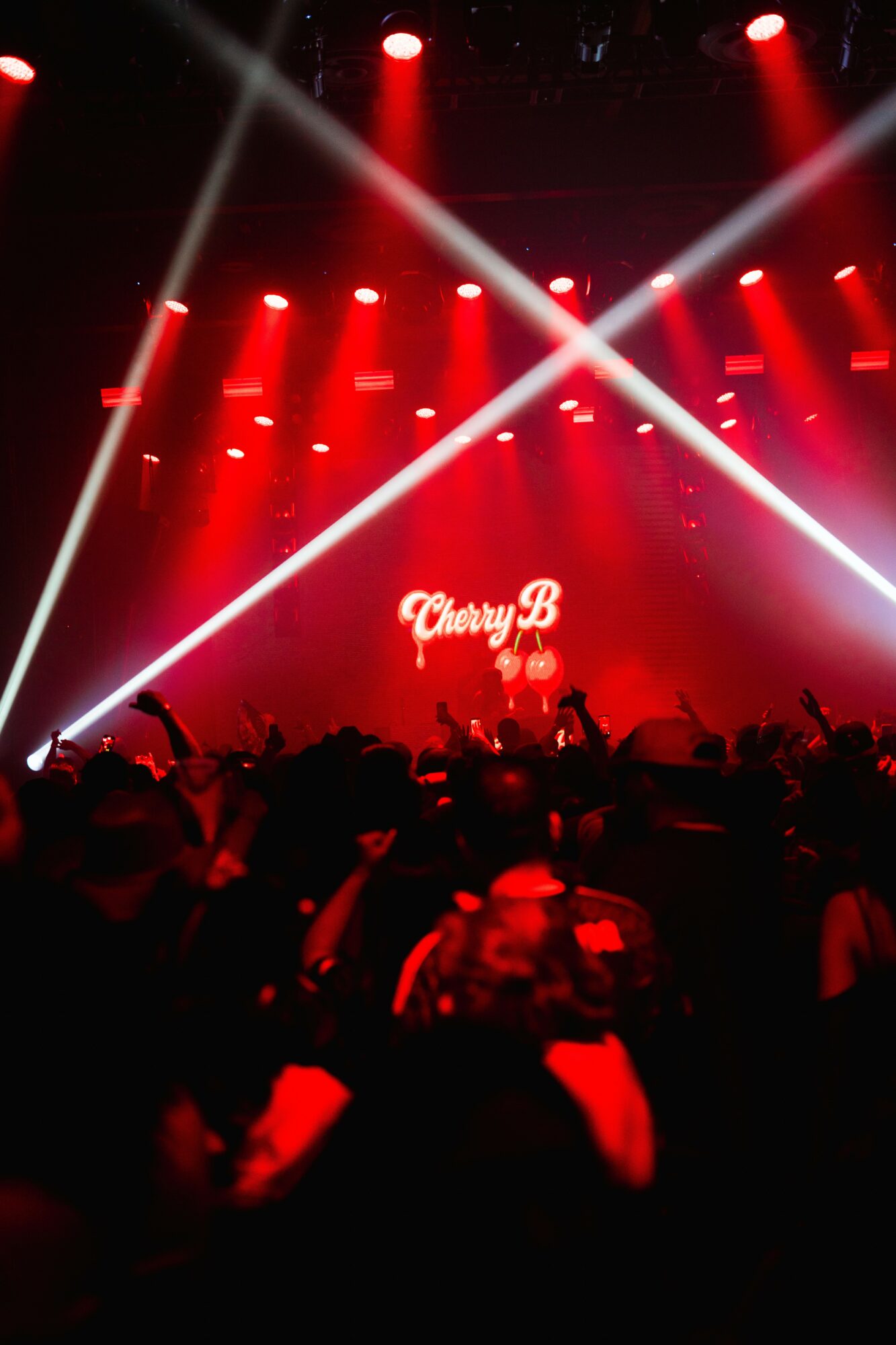 Concert stage with red lighting, beams of white light, and a sign reading 'Cherry B' in the background.