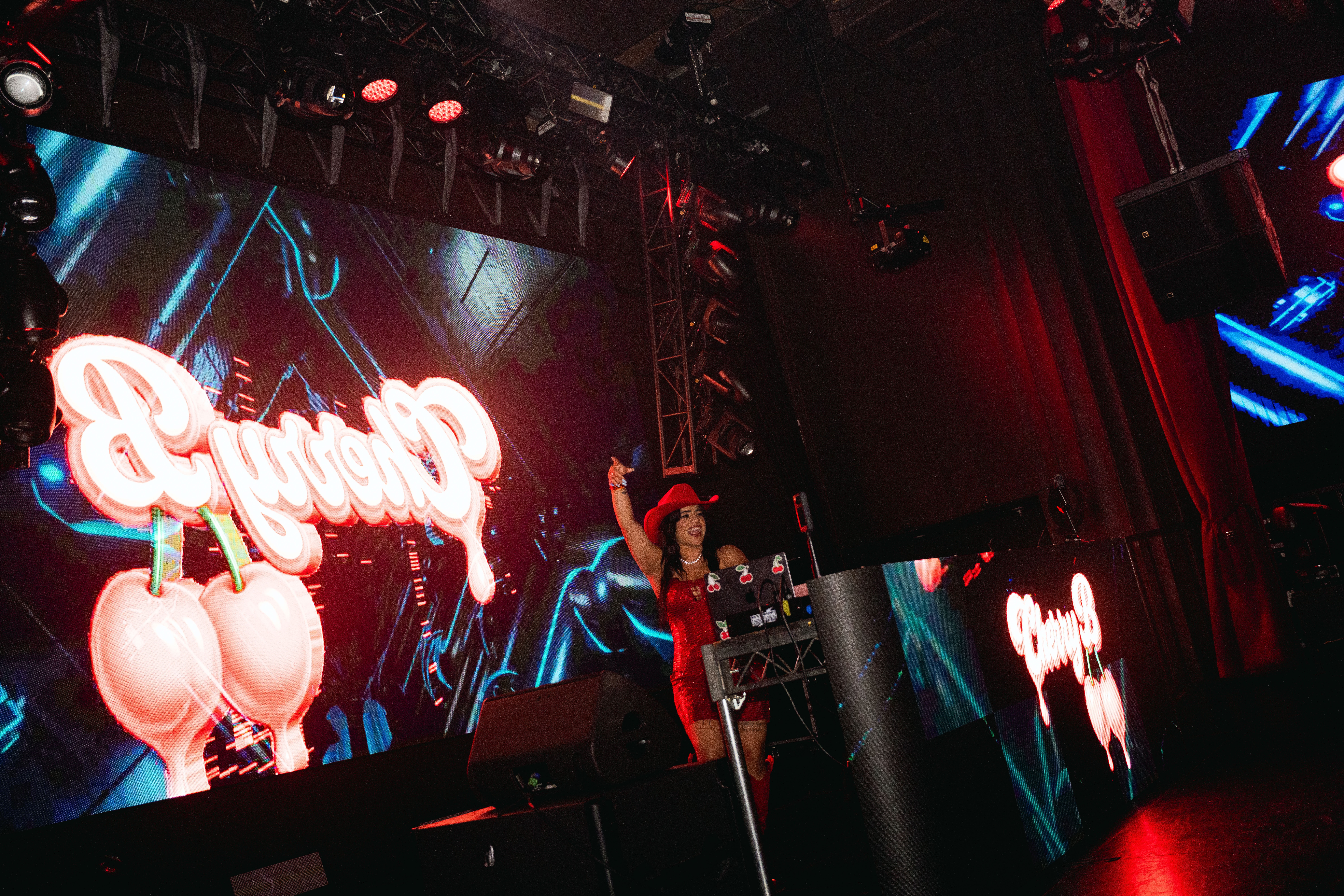 Performer on stage with large illuminated sign and digital background, holding a microphone, in a concert setting.