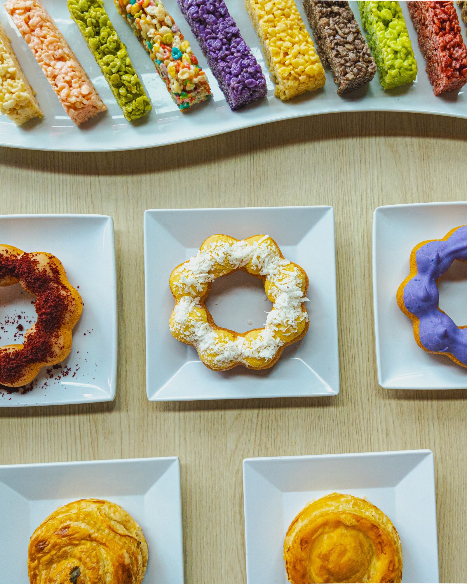 Six colorful candy sticks at the top, three donuts on white plates below, on a light wooden surface.
