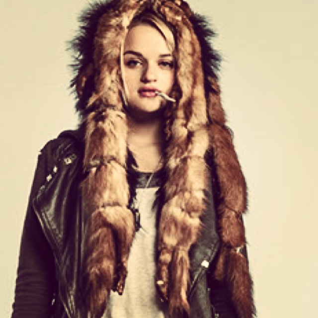 Young woman with long hair wearing a fur-lined hood and leather jacket, looking at the camera.