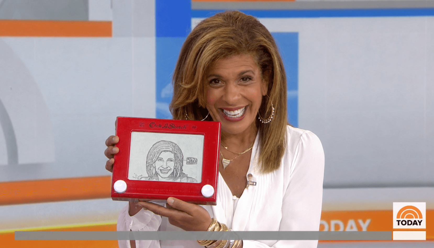 Woman with shoulder-length hair smiling and holding a framed drawing, in a studio setting.