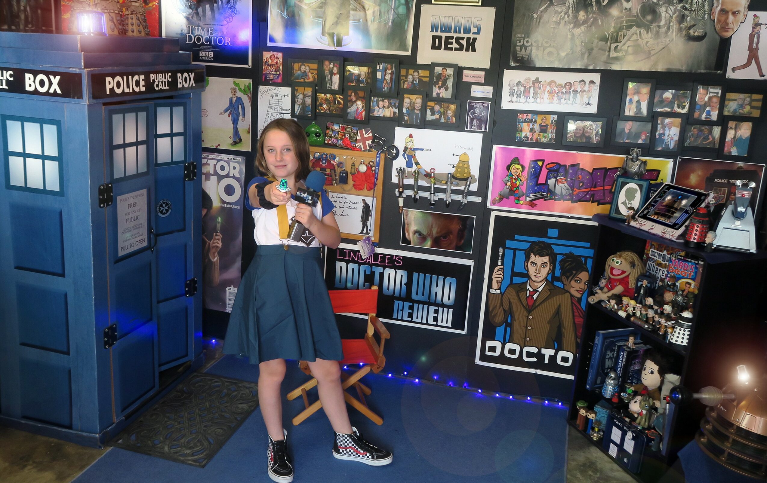 Girl in a blue dress and sneakers standing in front of Doctor Who-themed display with TARDIS and posters.
