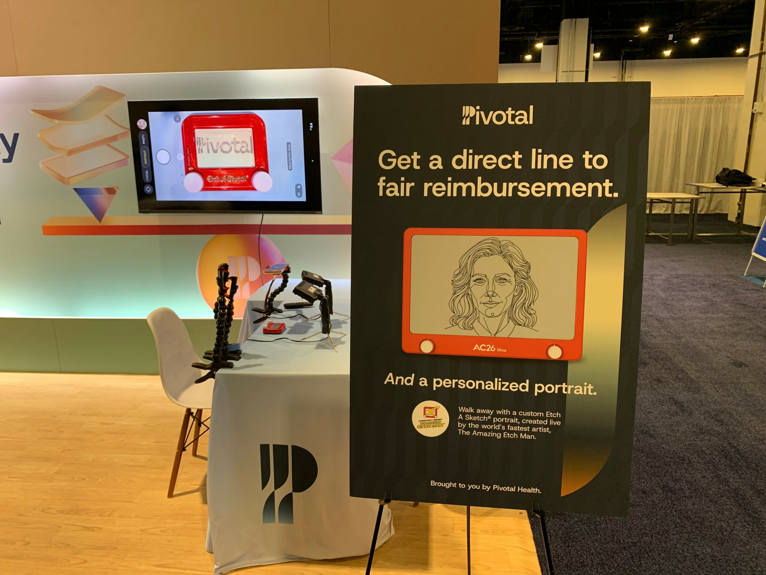 Display booth with a screen and promotional sign about personalized portraits and reimbursement, at an indoor event.