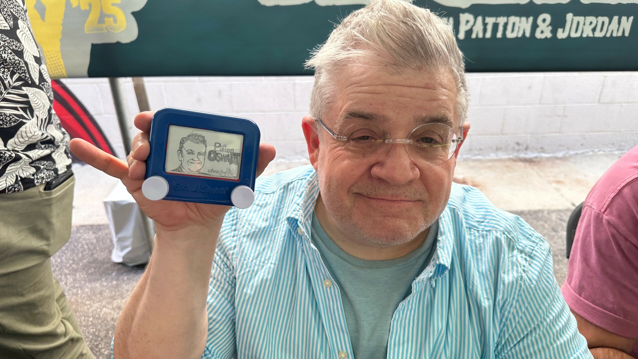 Older man with glasses and gray hair holding a small blue device with a face on the screen, smiling.