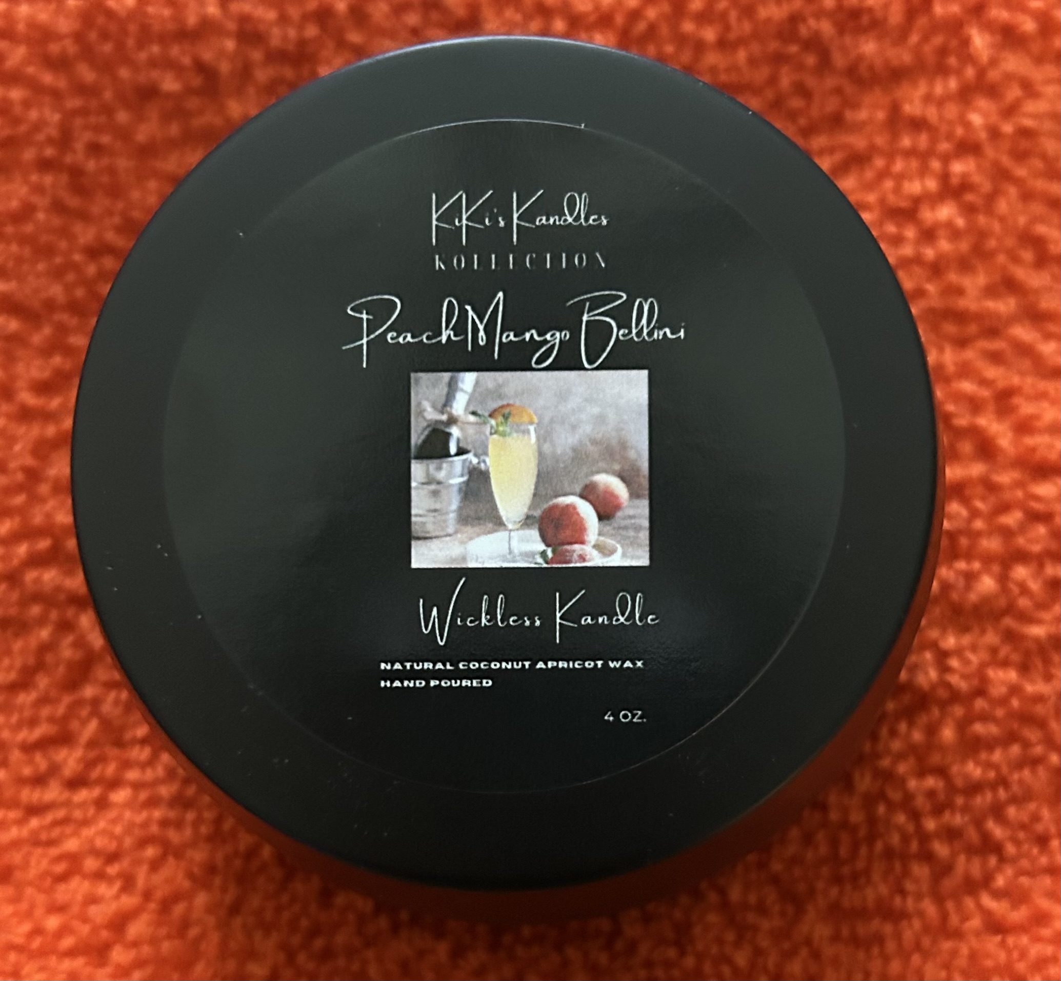 Round black container with a label featuring a glass of peach Bellini and peaches, on a red textured background.