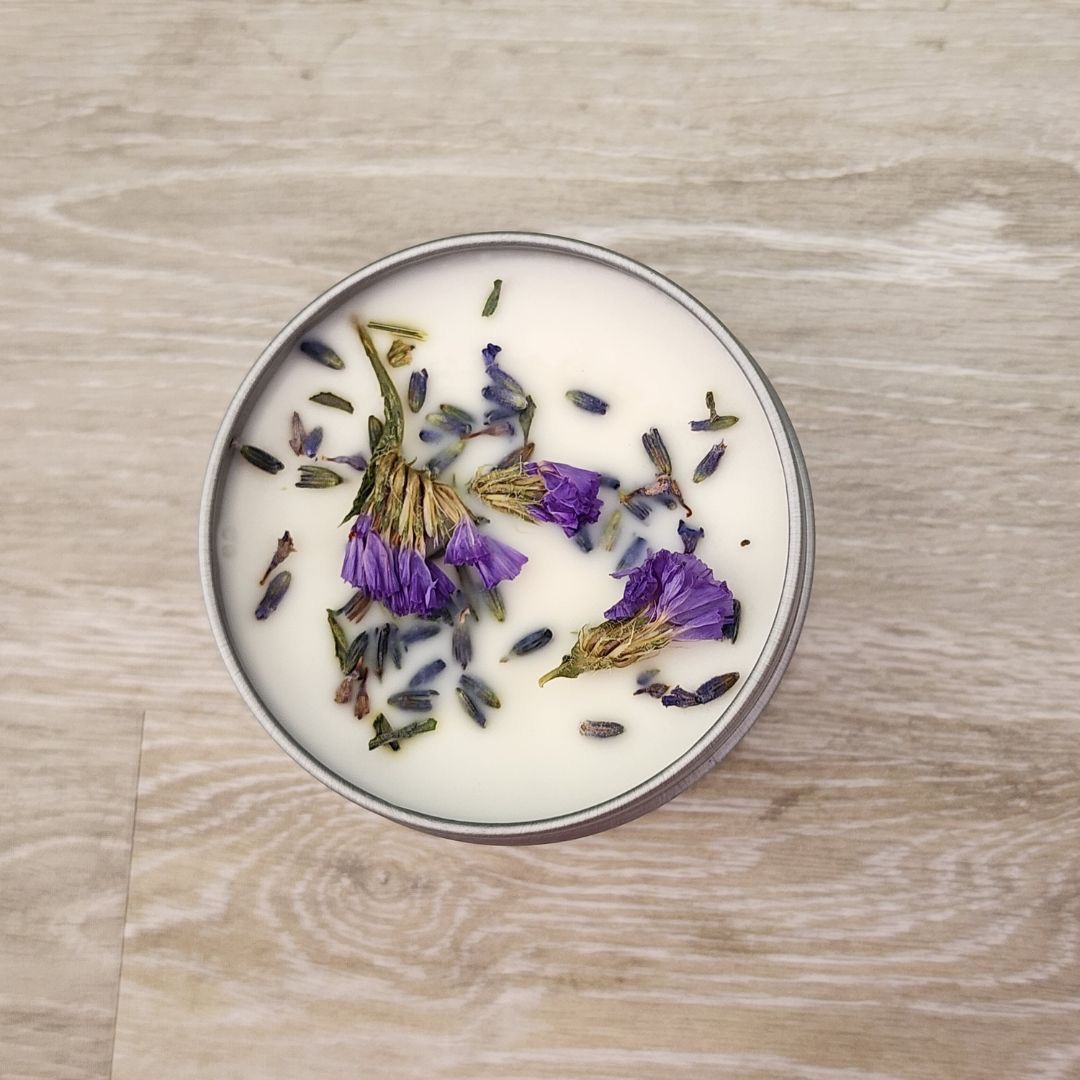 A round container with purple and green dried flowers floating in a white liquid, on a wooden surface.