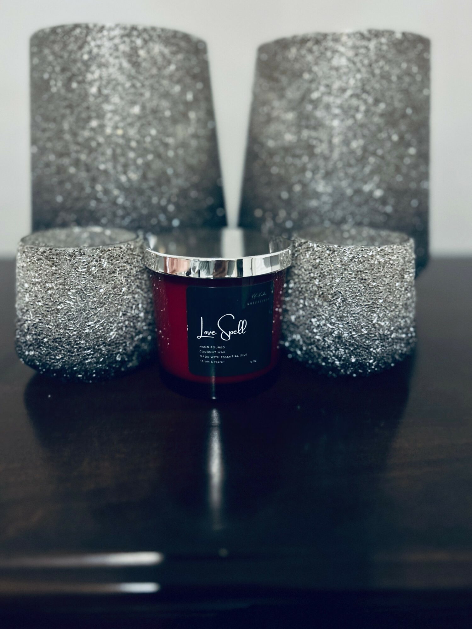Four glittery silver candles and a red jar with a silver lid on a dark surface.