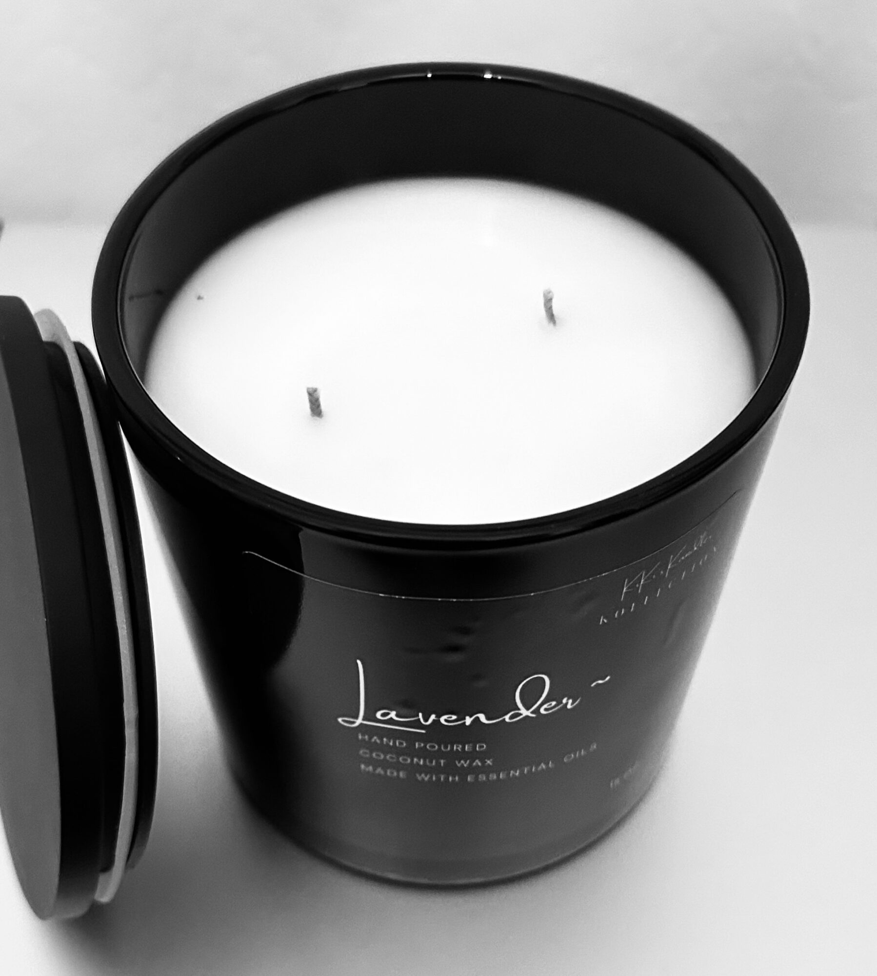 Black lavender-scented candle in a jar with a lid, label reading 'Lavender', on a light surface.