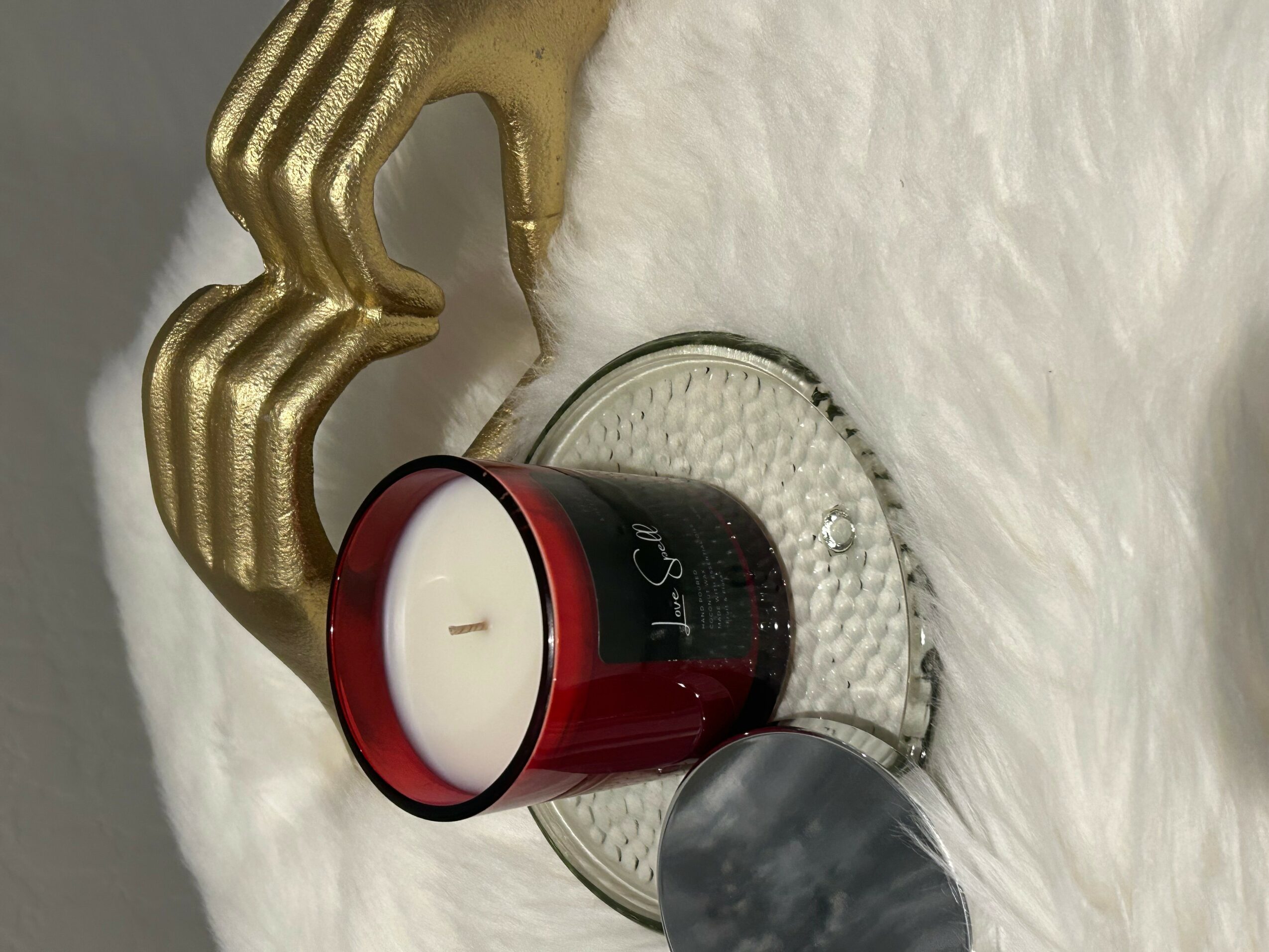 Red and white candle on a glass plate, with a gold decorative hand and white furry surface.
