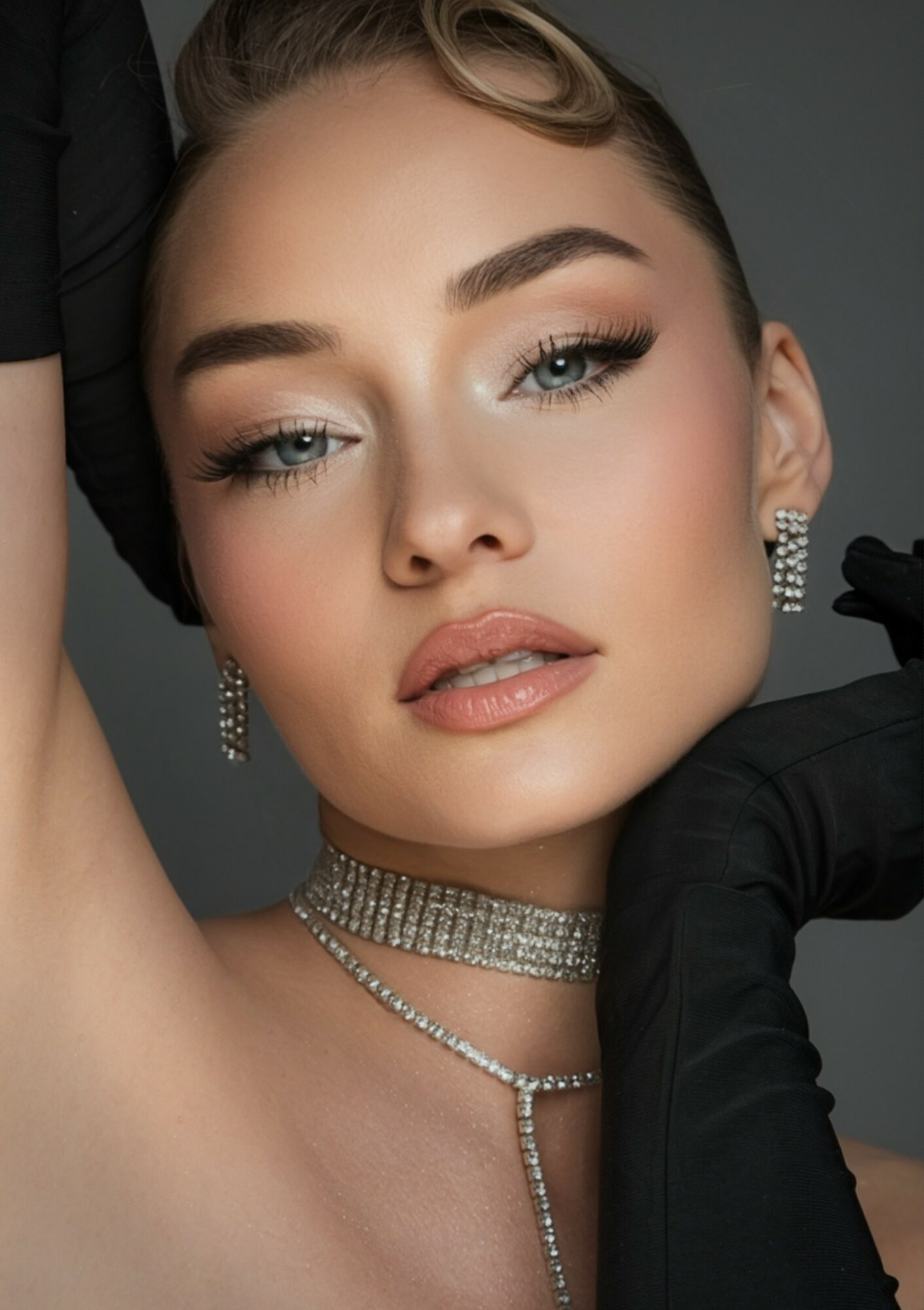 Close-up of a woman with styled hair, makeup, and jewelry, looking at the camera with a neutral expression.