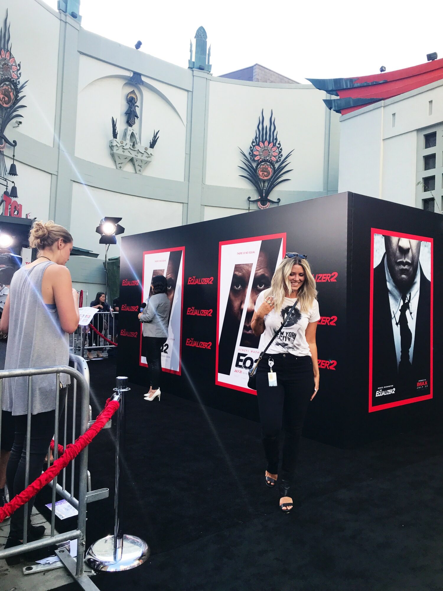 Woman standing in front of promotional display with images of a man, at an outdoor event, with a white building in background.