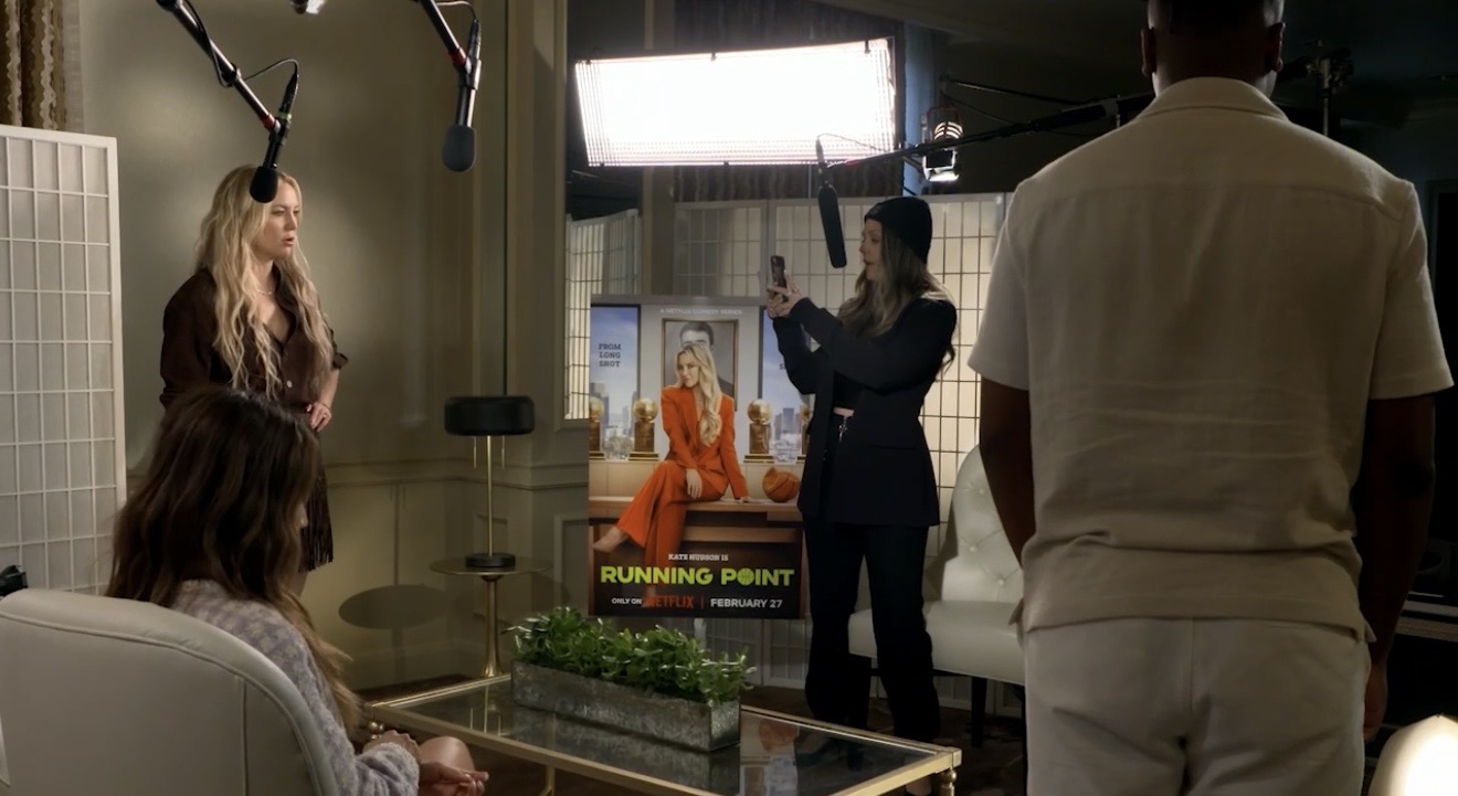 People in a recording studio with a woman on a screen, a person holding a boom mic, and others observing.