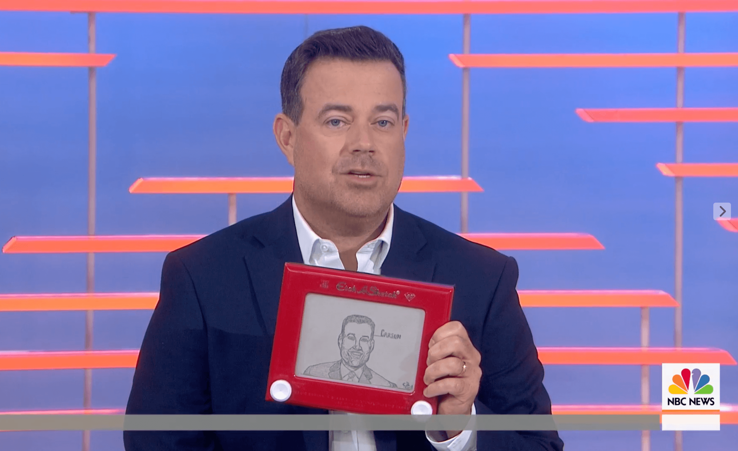 Man in suit holding a framed drawing on a TV set with colorful background.