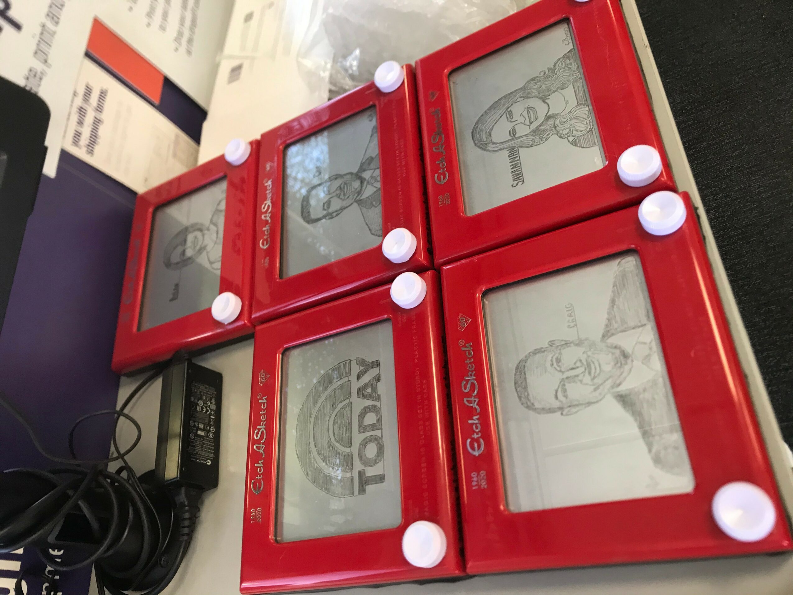 Four red digital photo frames with white buttons display sketches and a woman, placed on a surface with papers and cables nearby.