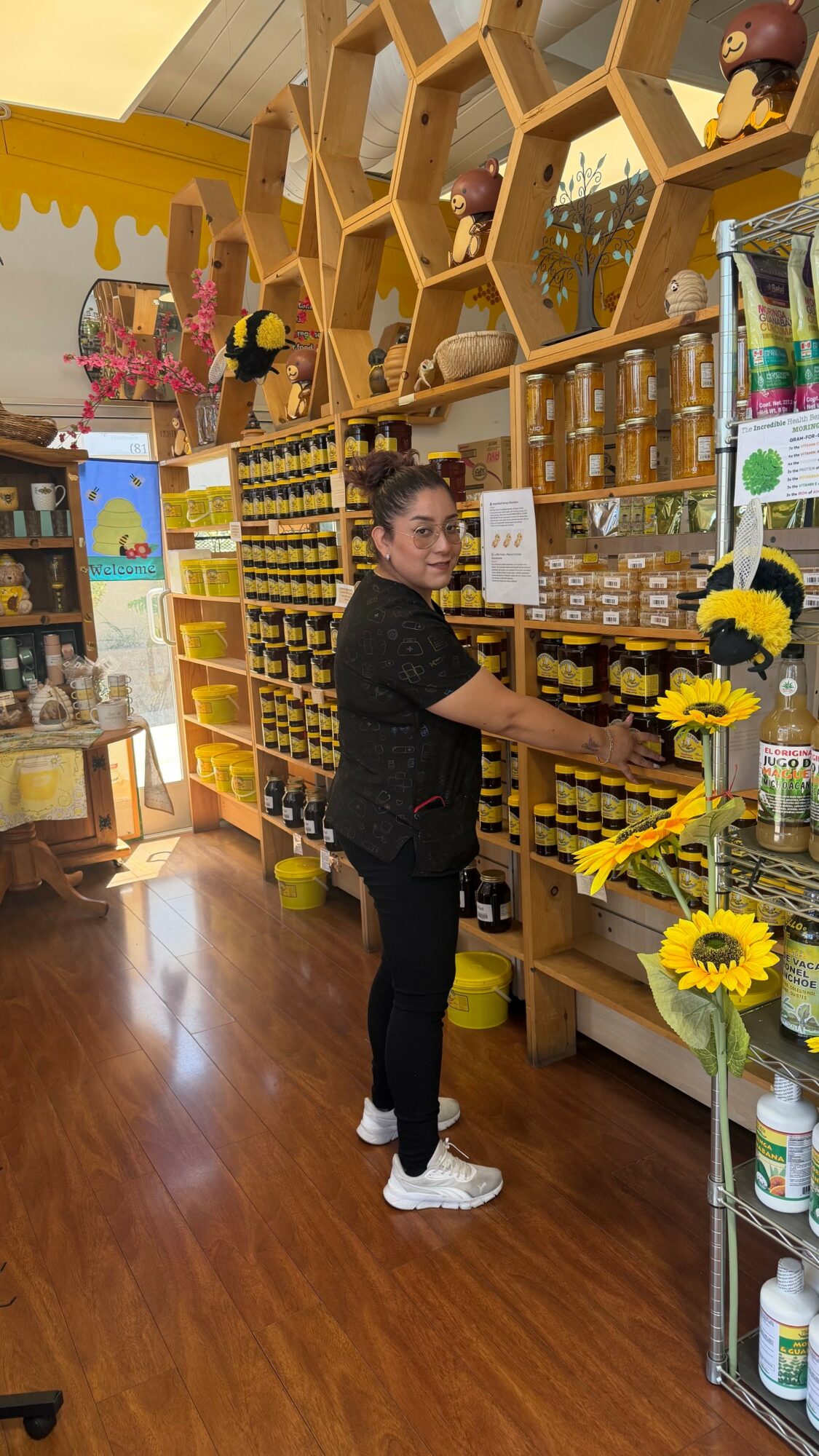 Woman shopping in a store with honey jars and sunflower decorations, honeycomb shelves, and bright yellow accents.