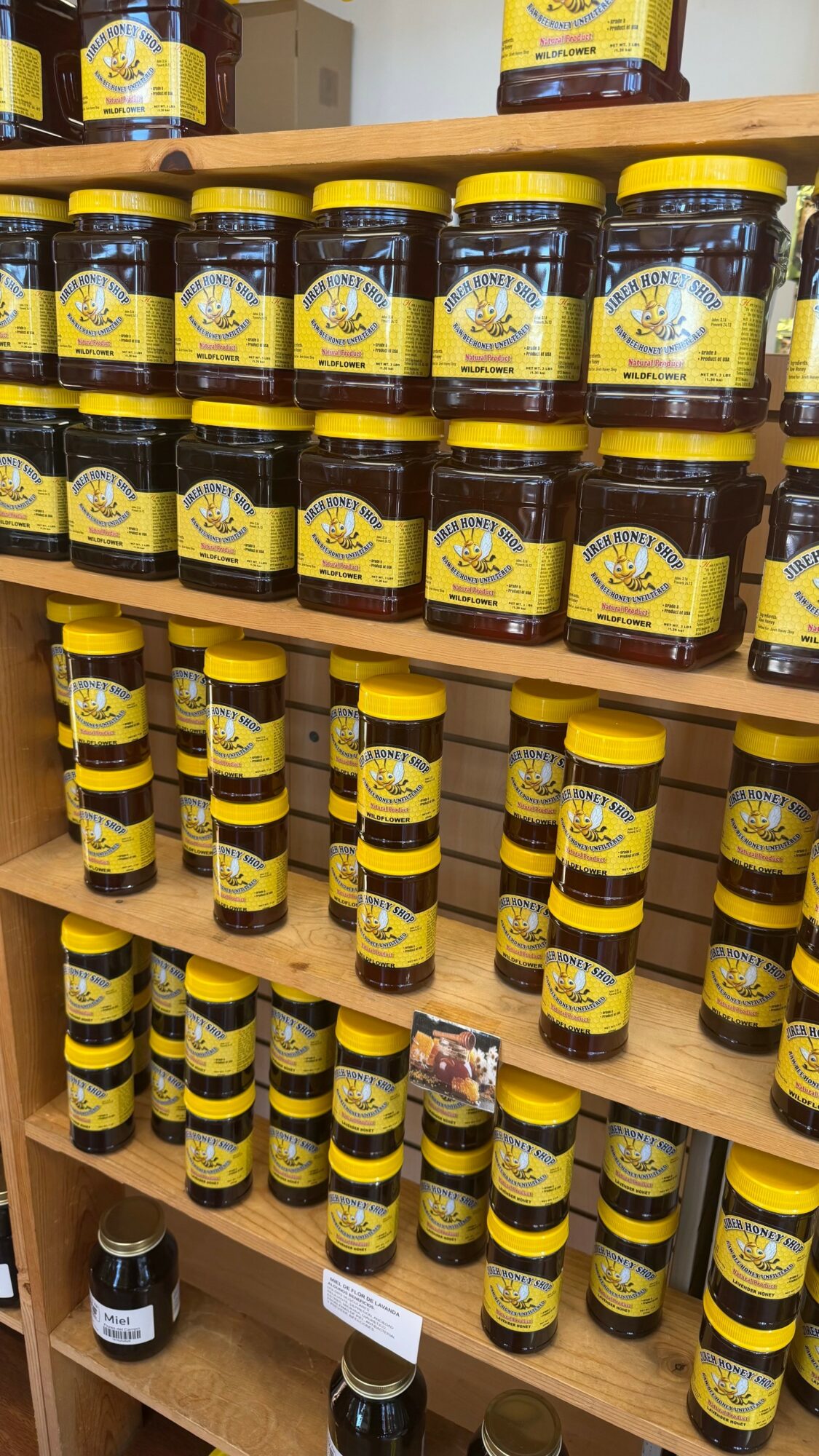 Multiple jars with yellow labels and black lids arranged on wooden shelves, with some jars stacked vertically.