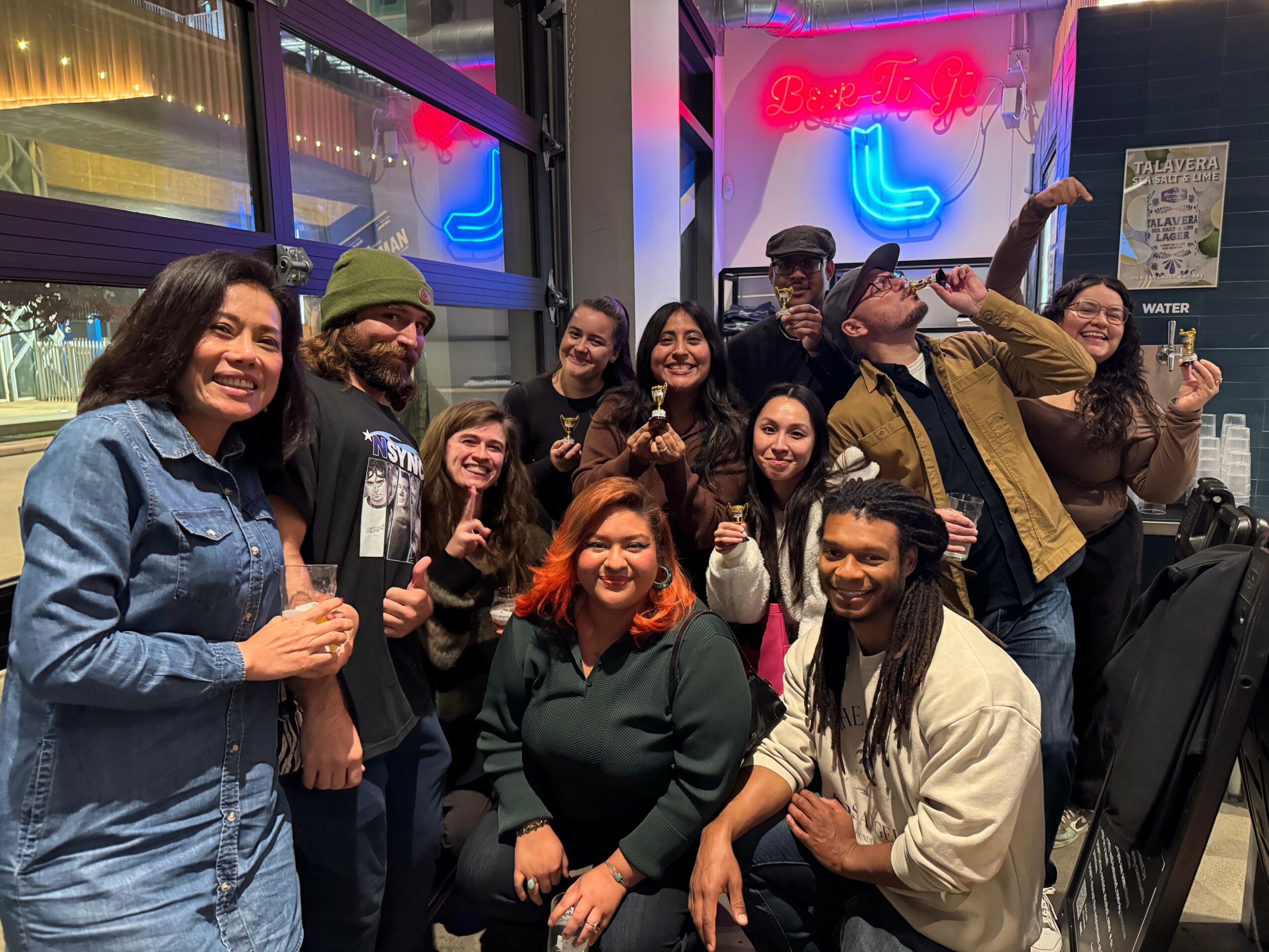 Group of people smiling and posing inside a restaurant with neon signs in the background.