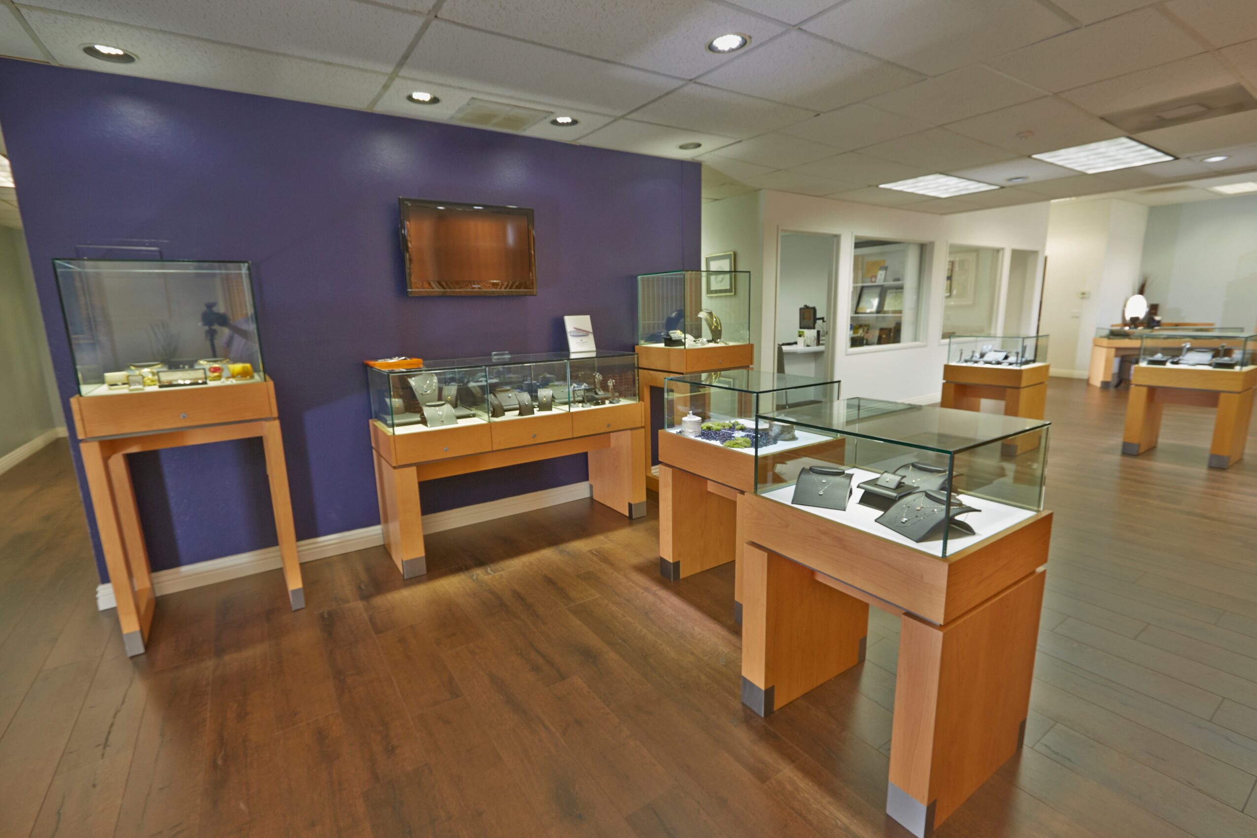 Museum display area with glass cases on wooden stands, a purple wall, and a flat-screen TV, with additional display tables in the background.