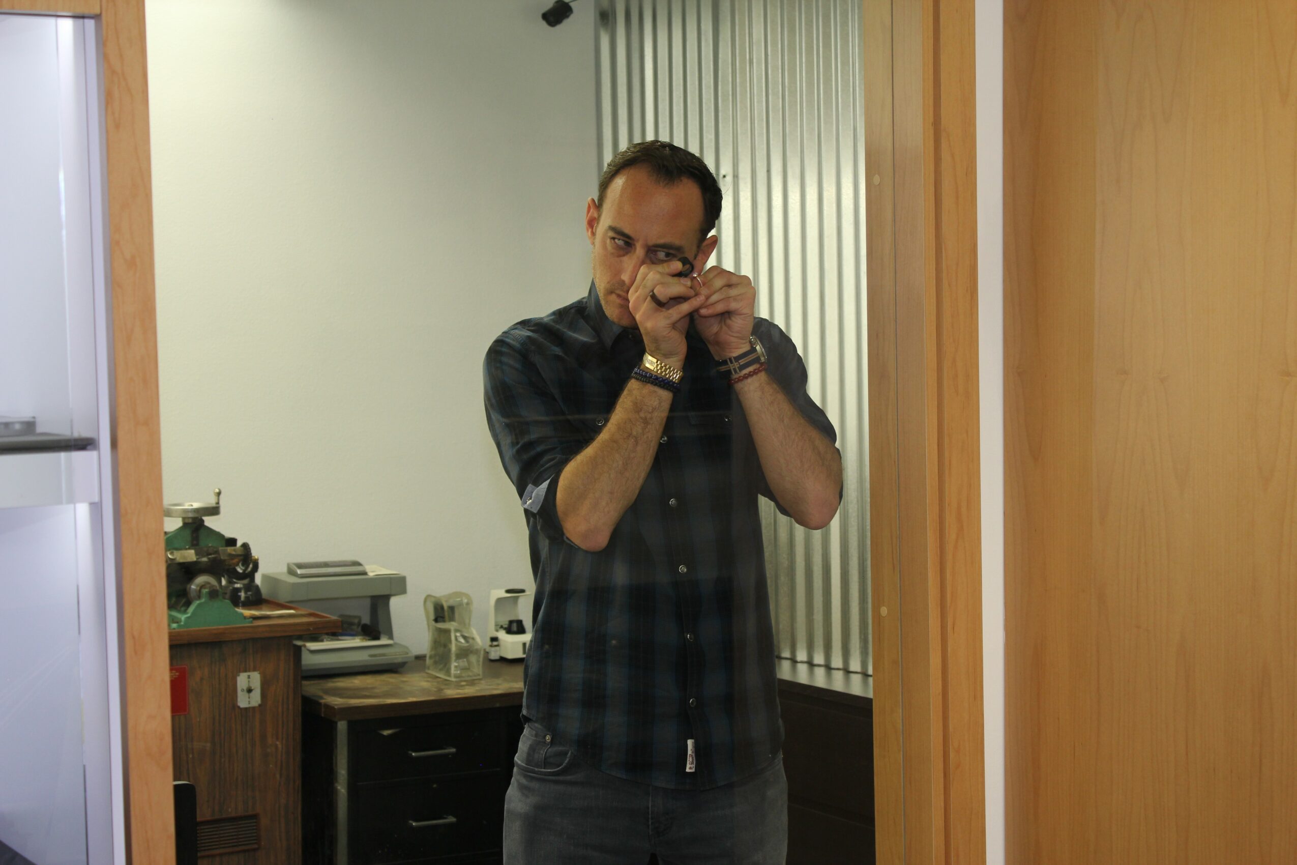 Man taking a photo in a mirror, wearing glasses and a dark plaid shirt, in a room with wooden furniture.