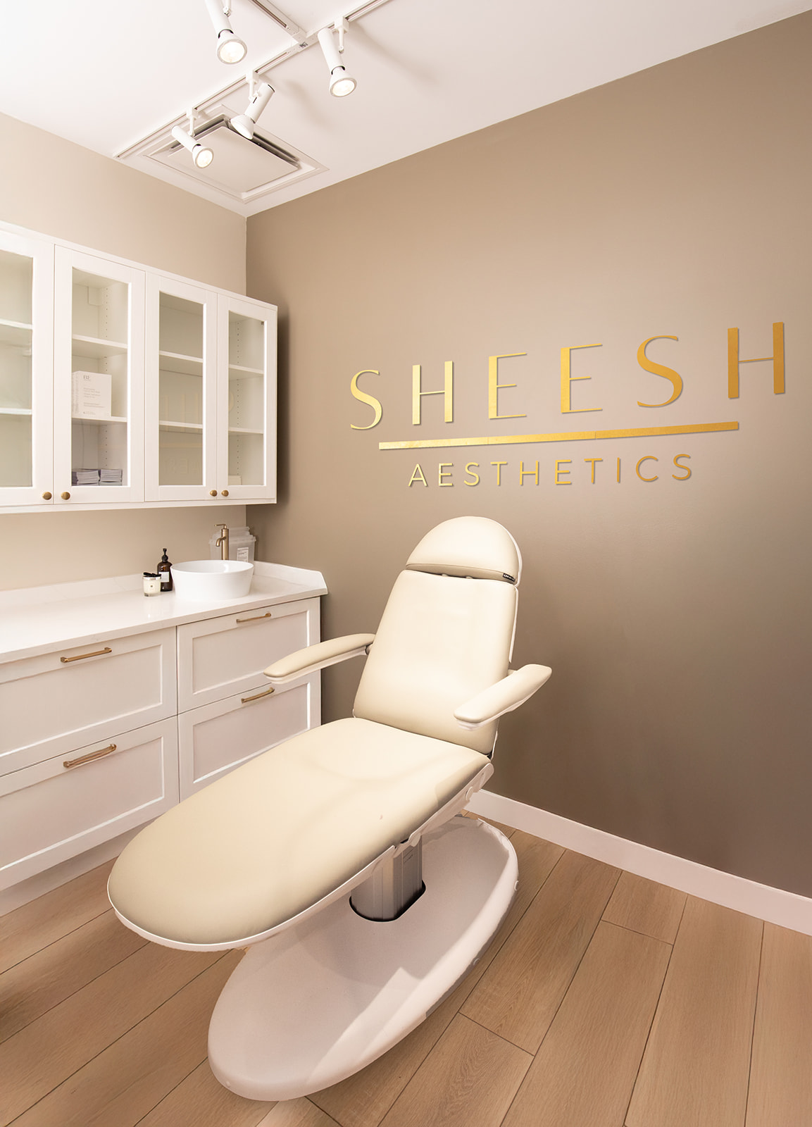 Treatment room with cream-colored chair, white cabinet, and gold lettering on beige wall, in a spa or clinic setting.