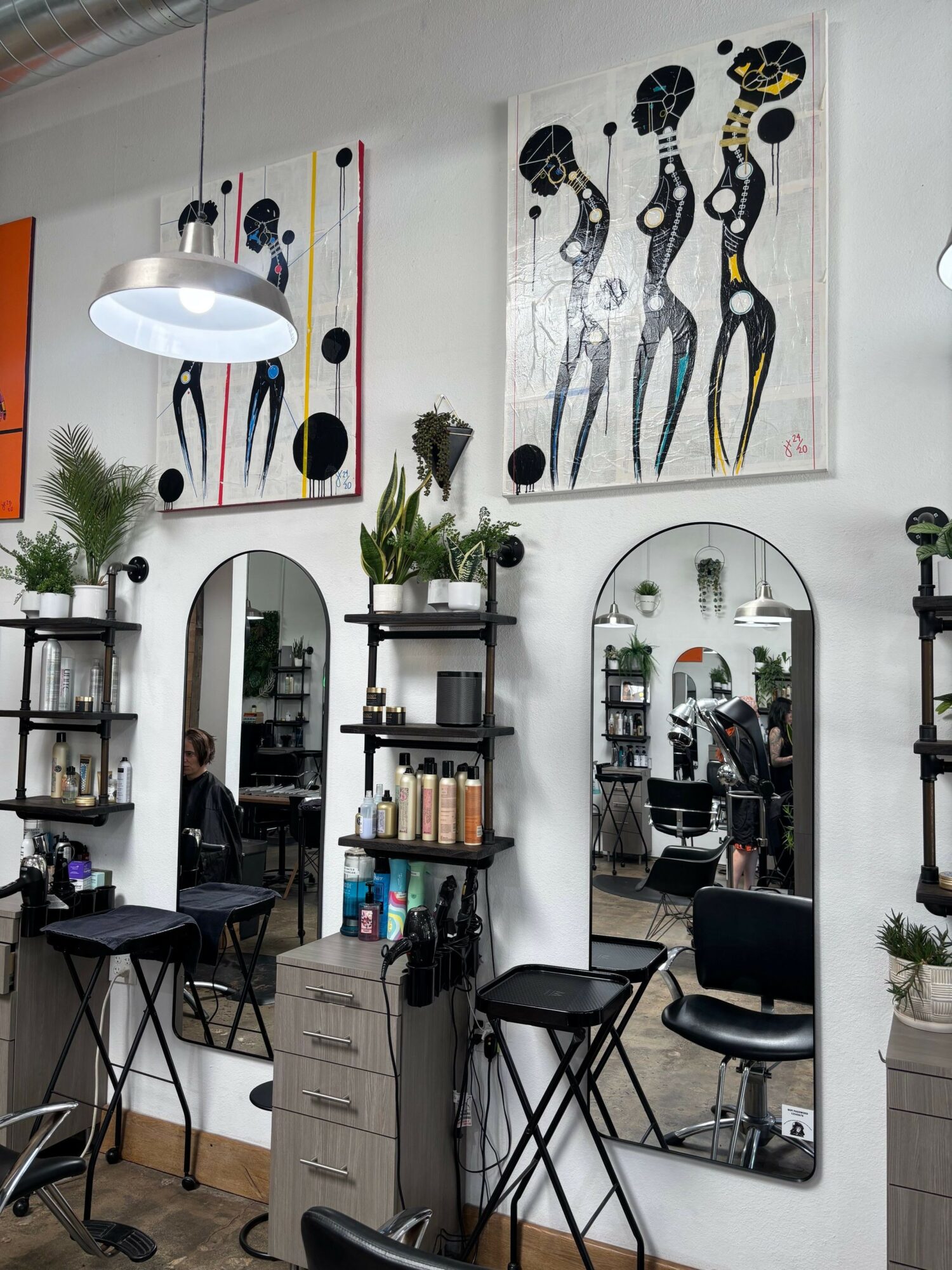 Interior of a modern salon with artwork, mirror, plants, and styling chairs, viewed from the side.
