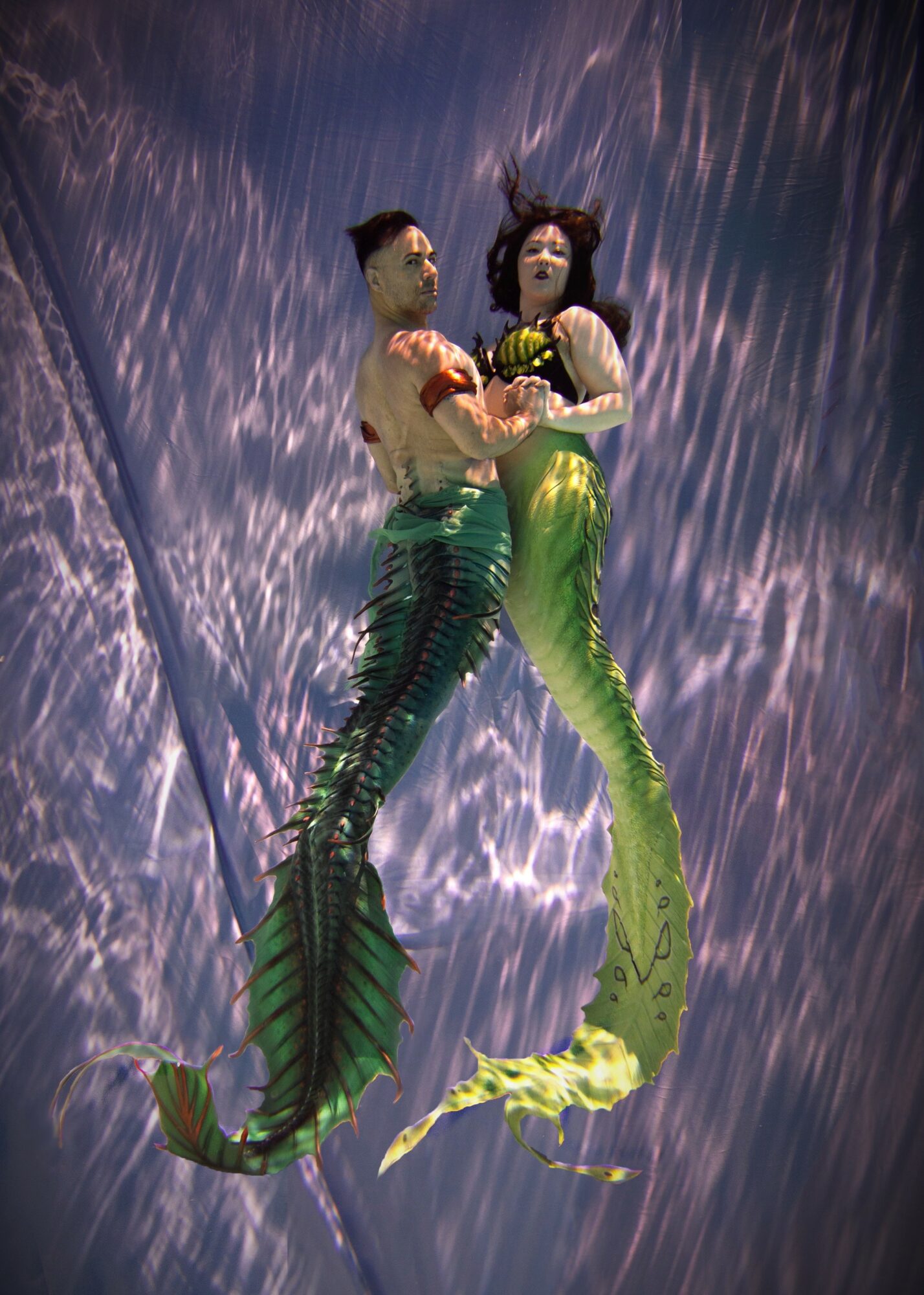 Two mermaid puppets with green tails and upper bodies, holding a yellow object, against a starry night sky background.