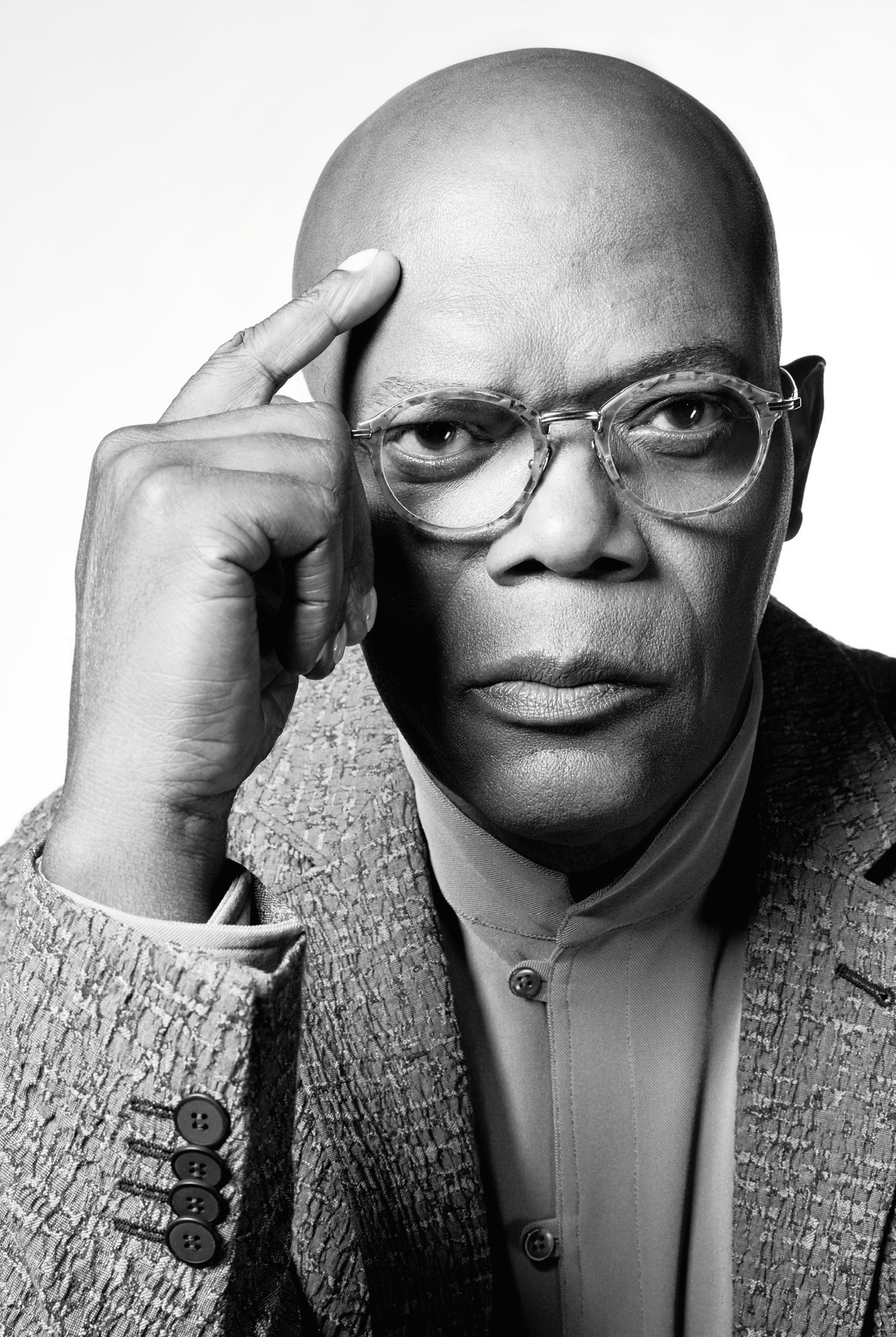 Black and white portrait of a person with glasses, bald head, wearing a suit, touching temple with index finger.