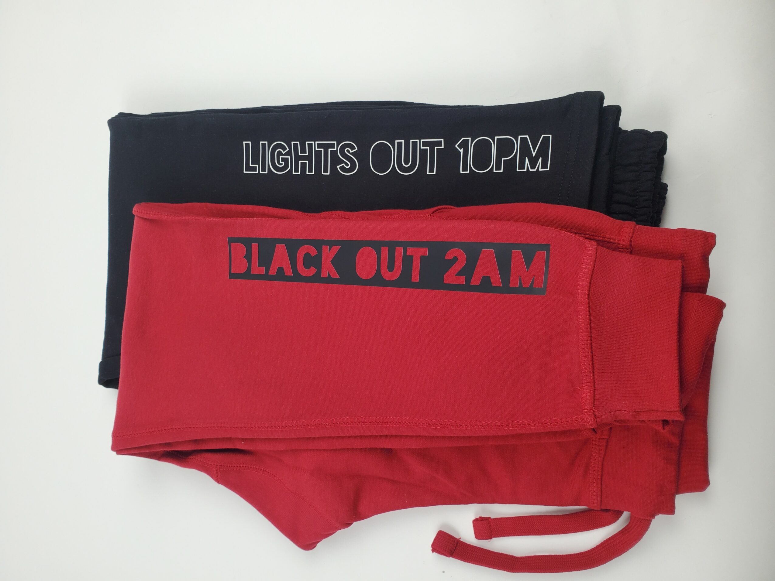 Two folded fabric masks, one black with white text and one red with black text, on a white surface.