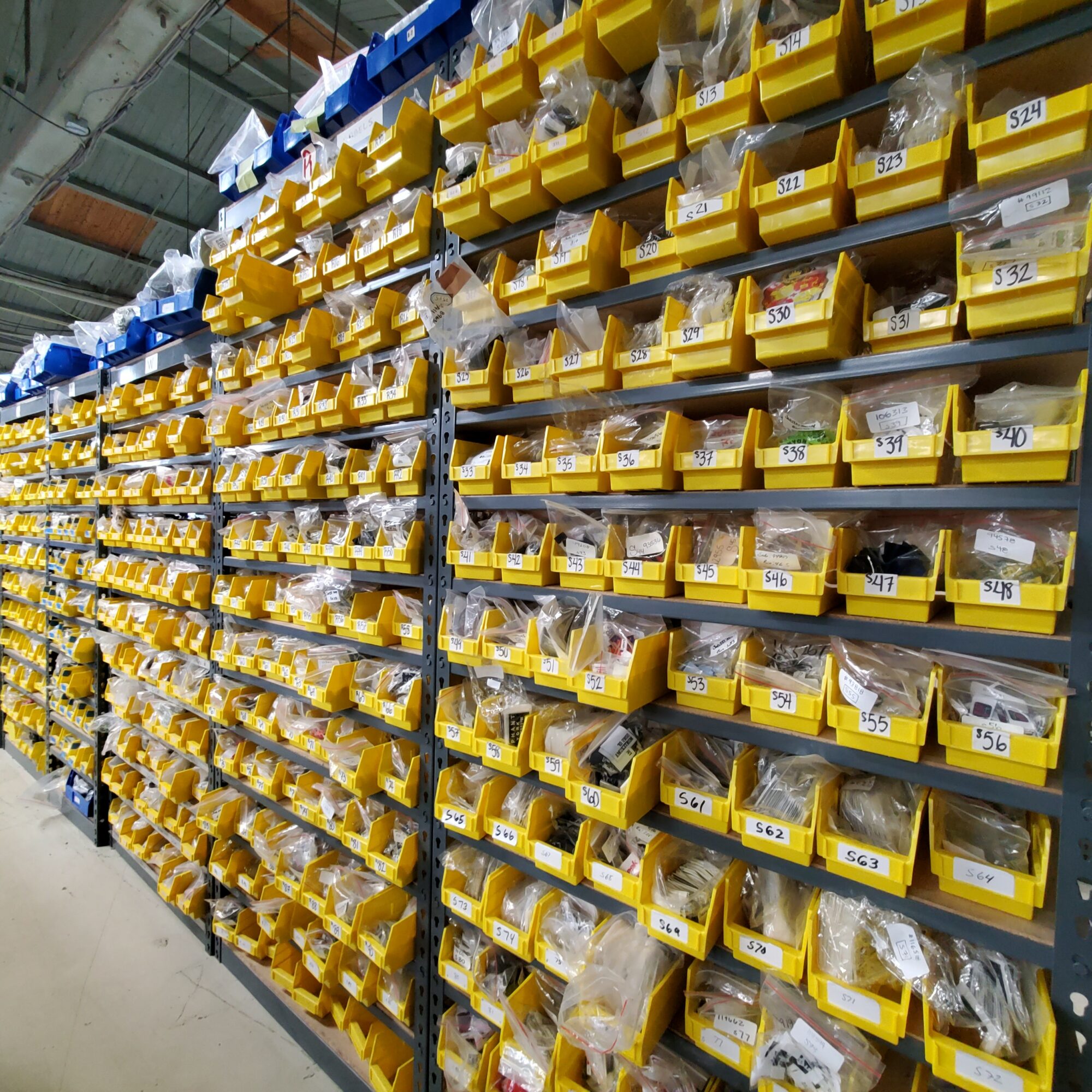 Shelves filled with yellow bins containing small hardware items in a store aisle.